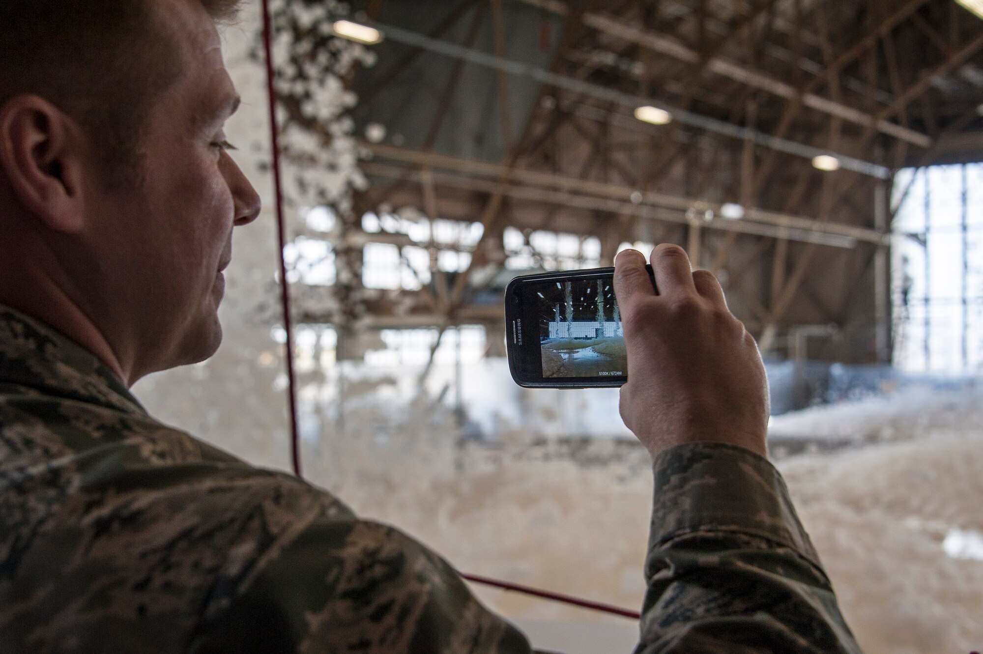 Capt. Gavin Johnson, 92nd Air Refueling Wing assistant staff judge advocate, uses his smartphone to capture fire suppression foam as it engulfs a maintenance hangar as part of a test of the installation’s high expansion foam discharge in the repair aircraft maintenance hangar April 8, 2015, at Fairchild Air Force Base, Wash. The test allowed the installation to assess whether the system was capable of meeting essential milestones required for full certification including covering at least 90 percent of the aircraft’s silhouette and covering the entire hangar floor with at least one meter of foam within four minutes. (U.S. Air Force photo/Staff Sgt. Benjamin W. Stratton)