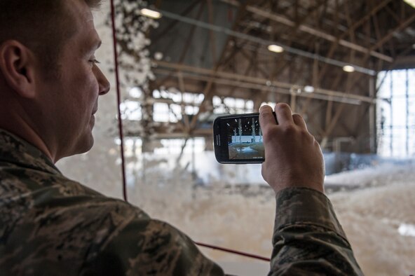 Capt. Gavin Johnson, 92nd Air Refueling Wing assistant staff judge advocate, uses his smartphone to capture fire suppression foam as it engulfs a maintenance hangar as part of a test of the installation’s high expansion foam discharge in the repair aircraft maintenance hangar April 8, 2015, at Fairchild Air Force Base, Wash. The test allowed the installation to assess whether the system was capable of meeting essential milestones required for full certification including covering at least 90 percent of the aircraft’s silhouette and covering the entire hangar floor with at least one meter of foam within four minutes. (U.S. Air Force photo/Staff Sgt. Benjamin W. Stratton)