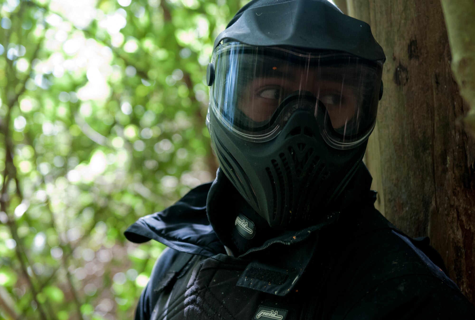 Senior Airman Armando Aparicio Jr., 65th Air Base Wing Public Affairs broadcaster, looks around a tree for members of the opposite team as he defends a flag at his base during a men's paintball trip, April 4, 2015. The chapel hosted this event as a way for Airmen to have fun in a safe and clean environment and to increase resiliency in the physical, social and spiritual domains of the RUFit? model. (U.S. Air Force photo/Staff Sgt. Zachary Wolf)
