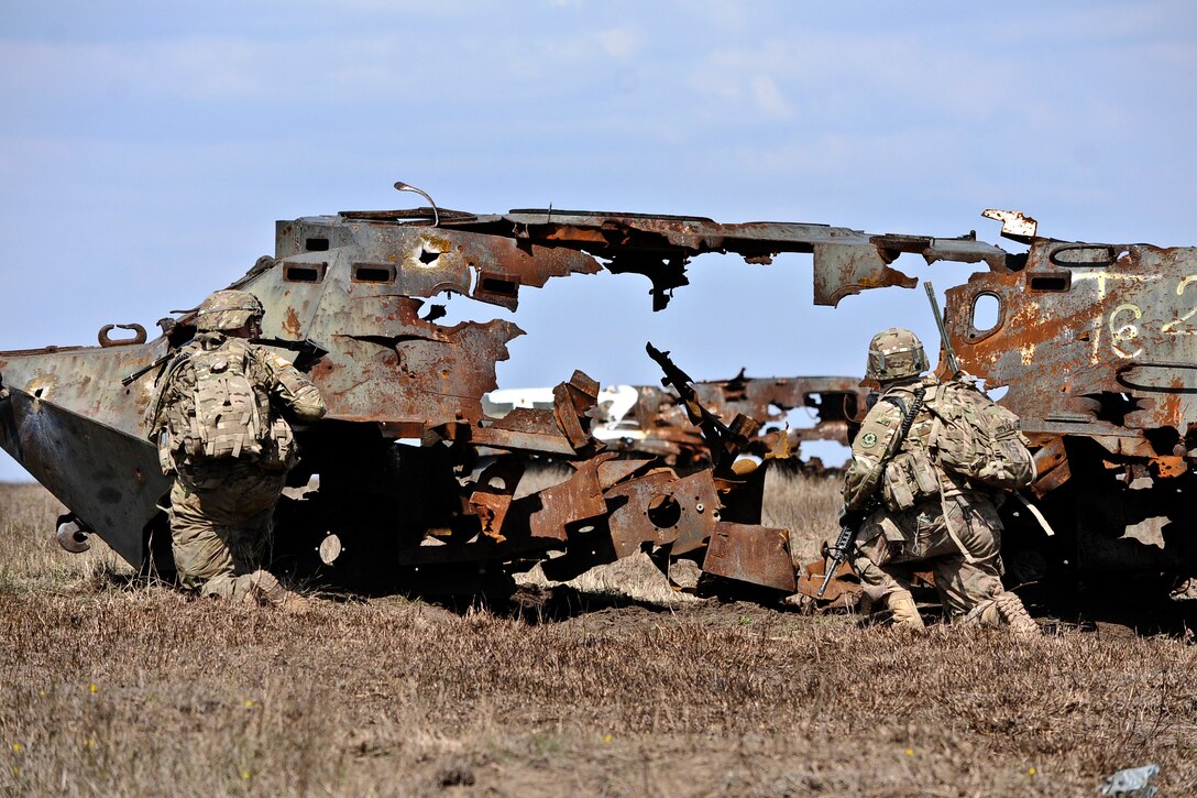 U.S. soldiers take cover behind an old military vehicle before moving toward their next objective during a live-fire exercise in Romania, April 8, 2015.