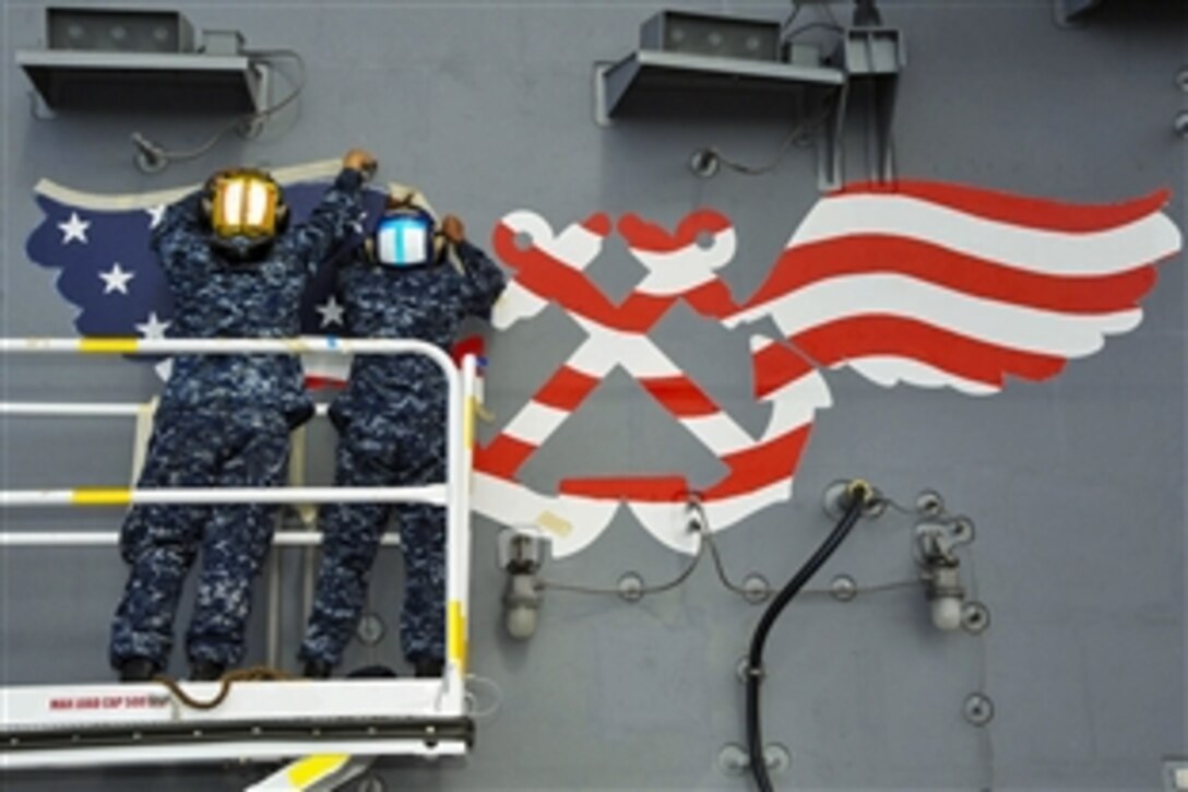 Navy Seamen Juan Gaviriacharry, left, and Ignacio Ramirez paint the aviation boatswain's mate wings onto the aircraft carrier USS Ronald Reagan in San Diego, April 7, 2015. The carrier is undergoing maintenance on Naval Base Coronado, Calif.