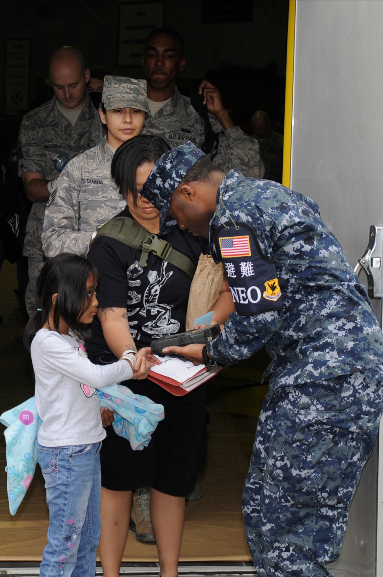 Dependants and other non-combatants have their identification bracelets scanned before entering a bus to be taken to a simulated aircraft during a Non-combatant Evacuation Operation exercise on Kadena Air Base, Japan, April 8, 2015. The non-combatants would be evacuated from the island to a safe location in the event of an emergency such as a severe typhoon. This exercise is intended to test how smoothly the NEO runs and what changes may need to be made. (U.S. Air Force photo by Staff Sgt. Marcus Morris)