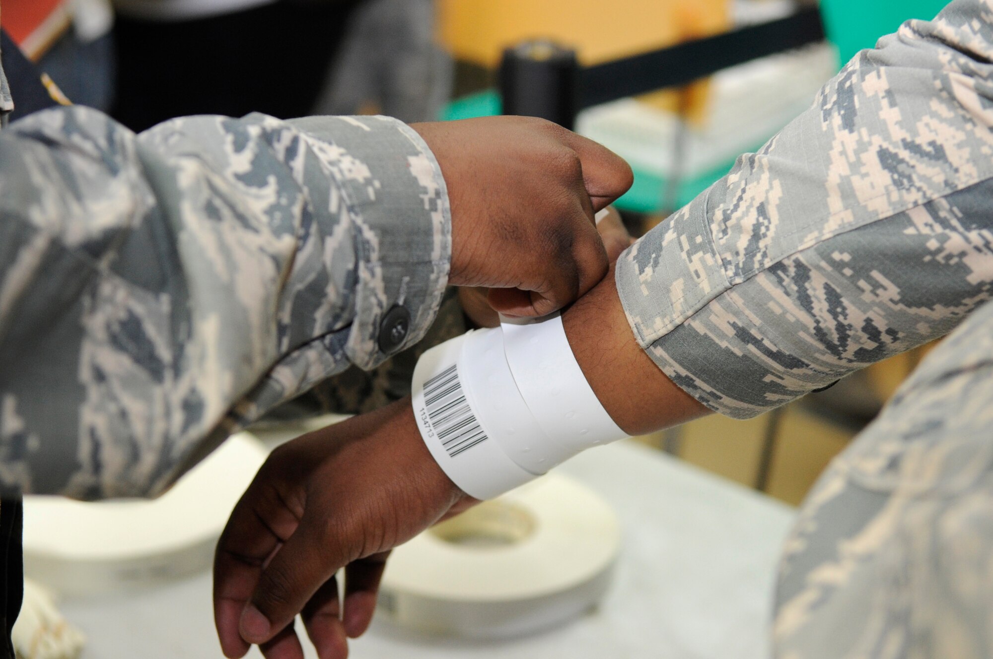 A U.S. Air Force 18th Wing member from the Non-combatant Evacuation Operation processing team places an identification bracelet on a volunteer representing a dependant on Kadena Air Base, Japan, April 8, 2015. The process is designed to update the NEO Travel System with proof that participants have completed each phase of the NEO process and are ready to board the designated mode of emergency transportation. (U.S. Air Force photo by Staff Sgt. Marcus Morris)
