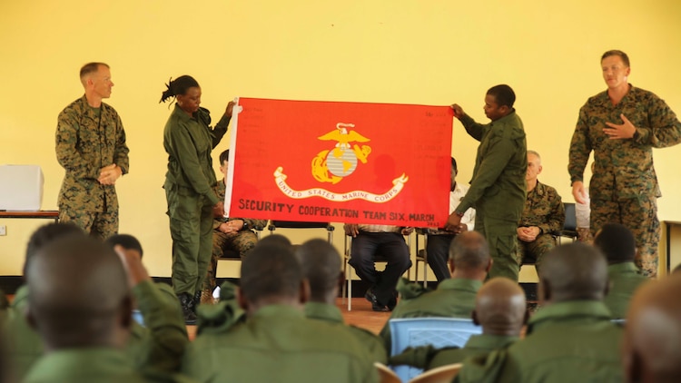 U.S. Marine Staff Sgt. Frederick Volz II (left) and Sgt. Kyle Kimbriel (right) present a Marine Corps flag to Tanzanian park rangers during a graduation ceremony on the Selous Game Reserve in Matambwe, Tanzania, March 27, 2015. Volz and Kimbriel are both members of a Security Cooperation Team with Special-Purpose Marine Air-Ground Task Force Crisis Response-Africa that spent four weeks teaching park rangers infantry skills in an attempt to help combat illicit-trafficking. 