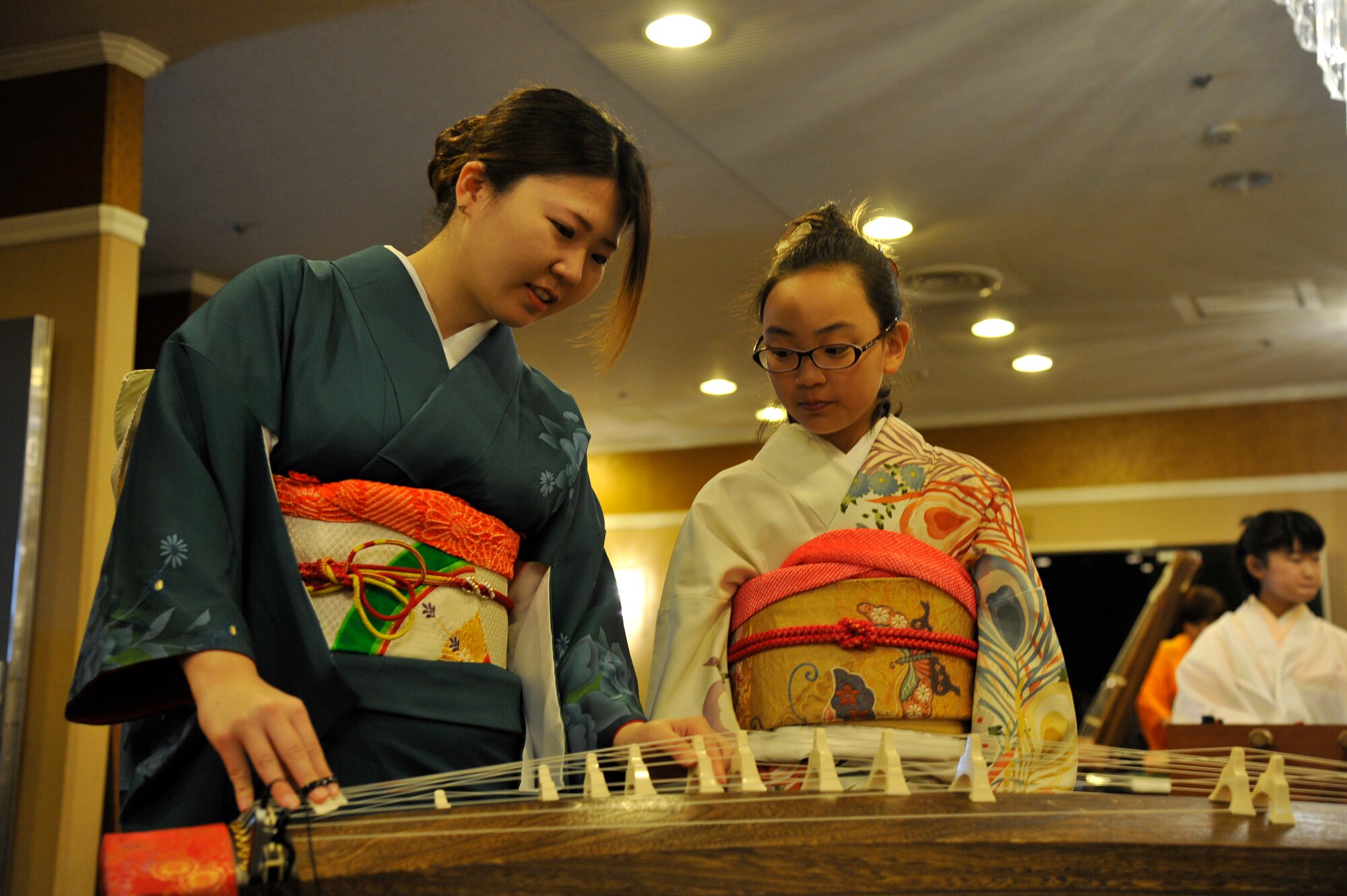 Two Japanese girls tune their koto, a traditional Japanese instrument, during Japan Day at Misawa Air Base, Japan, April 11, 2015. The girls, along with other volunteers, showed their prowess by playing instruments like the koto, flutes and the popular taiko drums. (U.S. Air Force photo by Senior Airman Patrick S. Ciccarone/Released)