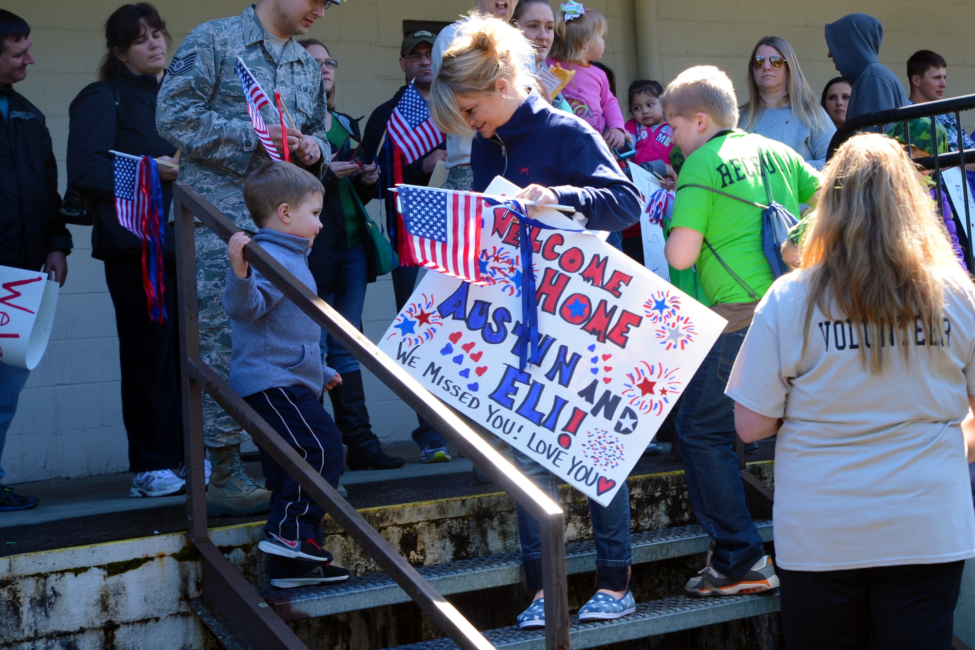 Parents wait with signs and flags for their children to return from a mock deployment at the conclusion of the Kids Understanding Deployment Operations event, April 11, 2015, at Joint Base Lewis-McChord, Wash. The children’s deployment, which lasted nearly two hours, included a pre-deployment briefing and a bus ride to a secret deployment location on McChord Field. (U.S. Air Force Photo/Senior Airman Rebecca Blossom)