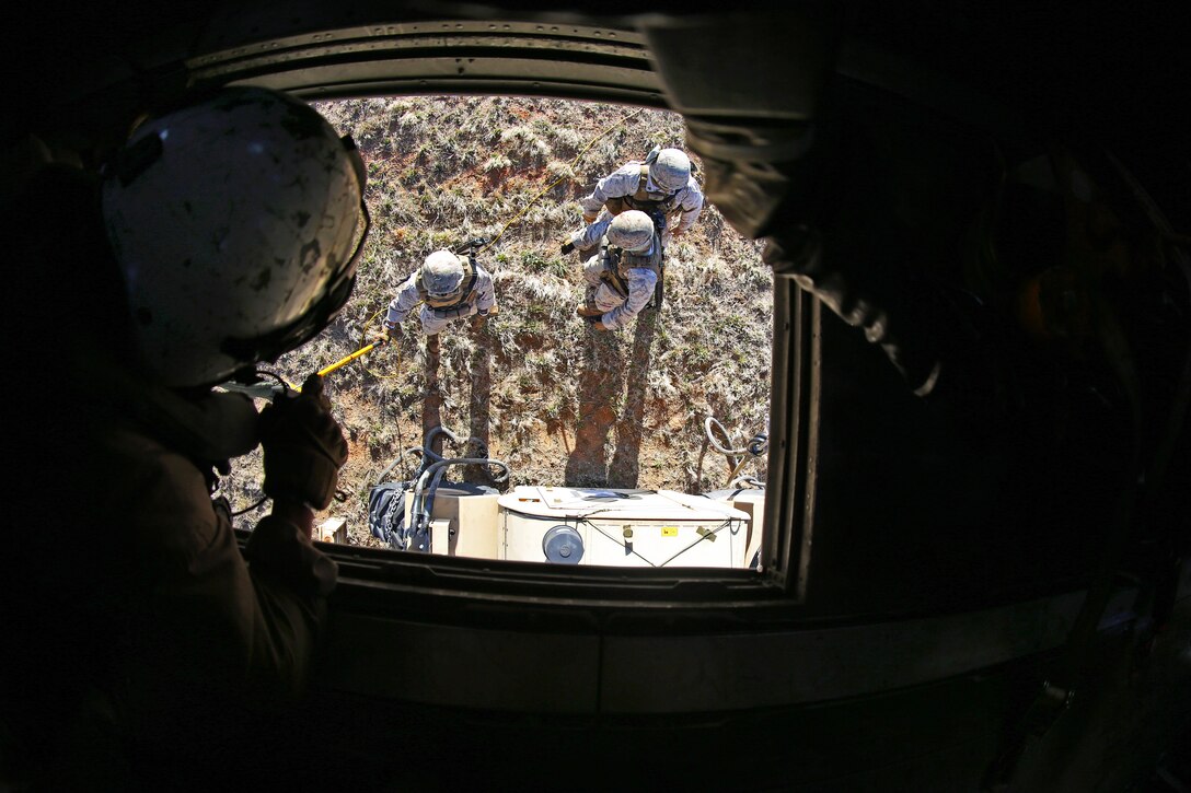 A Marine Corps crew chief, foreground left, watches from a helicopter as Marines on the ground secure chains from the helicopter to a forklift during helicopter support training on Fort Pickett, Va., April 11, 2015.