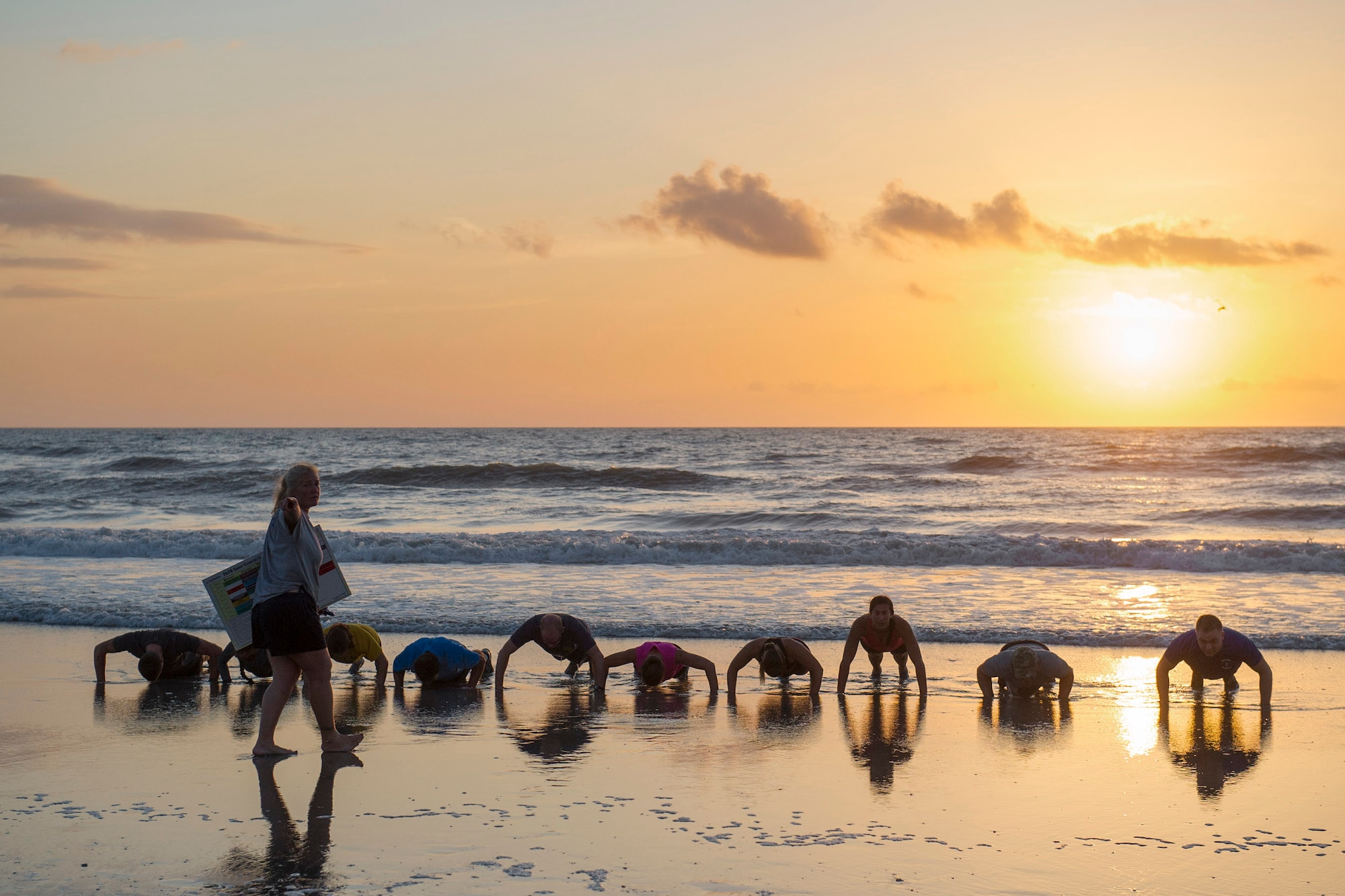 Members of the 45th Space Wing start off the 2015 Beach Endurance Race with push-ups in the Atlantic Ocean right outside of Patrick Air Force Base, Fla., April 10. Tammy Shelley, 45th Space Wing fitness and sports manager, holds a sign in preparation for team members to memorize their respective phrases to complete the race. (U.S. Air Force photo/Matthew Jurgens) (Released)