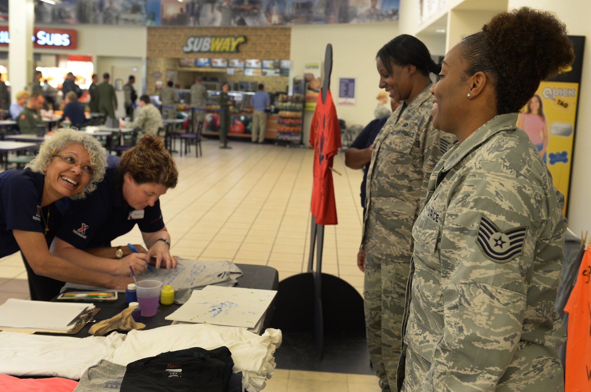Tech. Sgt. Coccara Evans, 628th Logistics Readiness Squadron unit deployment manager, and Tech. Sgt. Chiquica Frazier, 628th Logistics Readiness Squadron non-commisioned officer in charge flight service center, observe as two Base Exchange employees create a tee-shirt in support of Project Clothesline at the Base Exchange on April 13, 2015 at Joint Base Charleston, SC. Project Clothesline is a way for people affected by domestic abuse to express their feelings by decorating a tee-shirt and hanging it in a public area to encourage other victims to break the silence.  (U.S. Air Force Photo/Senior Airman Ericka Engblom)


