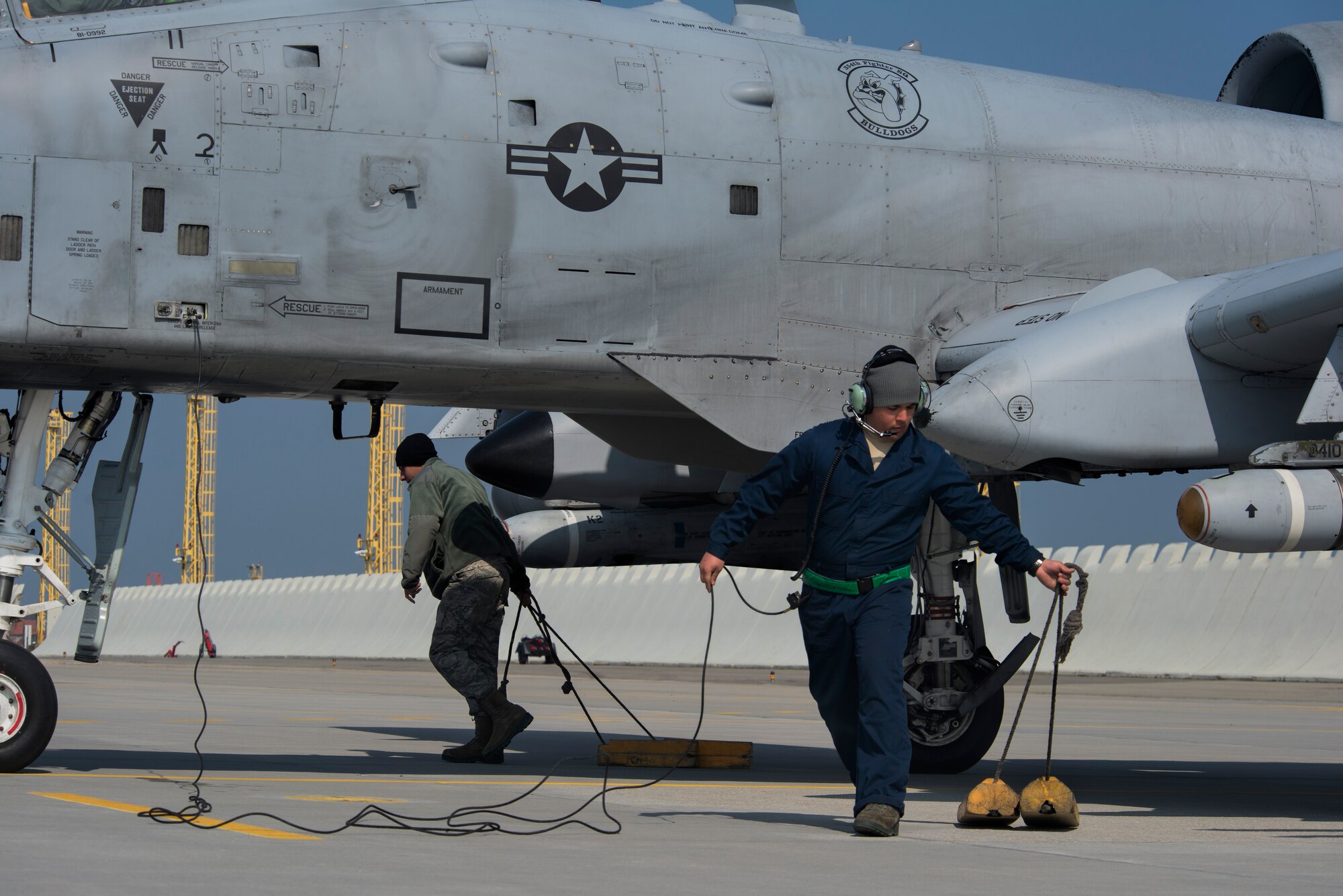 Aircraft maintainers assigned to the 354th Expeditionary Fighter Squadron remove the wheel chocks from under an A-10 Thunderbolt II attack aircraft’s tires in preparation for flight during a theater security package deployment to Namest Air Base, Czech Republic, April 10, 2015. More than 50 Airmen and support equipment from the 355th Fighter Wing, Davis-Monthan Air Force Base, Ariz., and the 52nd Fighter Wing at Spangdahlem Air Base, Germany, are here supporting this deployment. (U.S. Air Force photo by Staff Sgt. Christopher Ruano/Released)