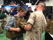 A Marine helps an attendee try on a plate carrier vest at the Gruntworks Squad Integration Facility display April 13 at the Sea-Air-Space Expo at National Harbor, Maryland. Marine Corps Systems Command's Marine Expeditionary Rifle Squad Team brought several systems and pieces of equipment to the expo to show attendees how they're working to reduce the Marine combat burden. (U.S. Marine Corps photo by Monique Randolph)