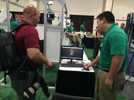 Evan Luo (right), an engineer on Marine Corps Systems Command's Marine Expeditionary Rifle Squad Team, explains the 3DMD imaging system to an attendee at the Sea-Air-Space Exposition. The MERS team uses the system to capture head measurements to inform design decisions for future helmets. The 3DMD was one of several systems and equipment MERS brought to the expo to show attendees how they're working to reduce the Marine combat burden. (U.S. Marine Corps photo by Monique Randolph)