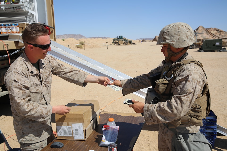 Sgt. Tyler Sylvester, troop morale specialist, Headquarters Battalion, hands change to Lance Cpl. Michael Seabolt, chemical, biological, radiological and nuclear specialist, 1st Transportation Support Battalion, after Seabolt made a purchase from the Mobile Tactical Field Exchange aboard Camp Wilson, April 13, 2015. (Official Marine Corps photo by Lance Cpl. Medina Ayala-Lo/Released)
