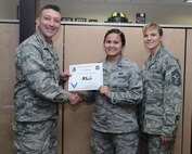 Airman 1st Class Ariel Delgado, center, 47th Flying Training Wing Public Affairs photojournalist, poses with Col. Brian Hastings, 47th FTW commander and Chief Master Sgt. Teresa Clapper, 47th FTW command chief, after accepting the XLer of the week award here April 8, 2015. The XLer is a weekly award chosen by wing leadership and was presented to Delgado for filling a Staff Sgt. role for two months by determining news stories and base publication timeline. (U.S. Air Force photo by Airman Brandon G. May)(Released)