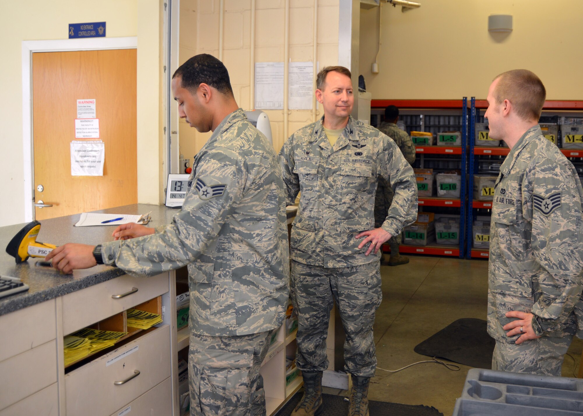 U.S. Air Force Senior Airman Corey Love, left, 100th Security Forces Squadron response force leader from Waldorf, Md., and U.S. Air Force Col. David Avila, center, 100th Mission Support Group commander, discuss post office procedures with U.S. Air Force Staff Sgt. Jeffrey Vanrees, 100th Communications Squadron postal clerk from Minot, N.D., as they spend time behind the parcel pick-up desk at the post office April 14, 2015, on RAF Mildenhall, England. Love spent the day with Avila as part of a job shadow event. The day included attending meetings, visiting 100th MSG workcenters and seeing what other Airmen do on a day-to-day basis. The new 100th MSG job shadow program allows Airmen from a squadron within the 100th MSG to spend a day with the commander. It provides an opportunity for Airmen to gain a greater perspective of the 100th MSG mission and show them how their role ties in with the mission of the group, the 100th Air Refueling Wing and U.S. Air Forces in Europe. (U.S. Air Force photo by Karen Abeyasekere/Released)