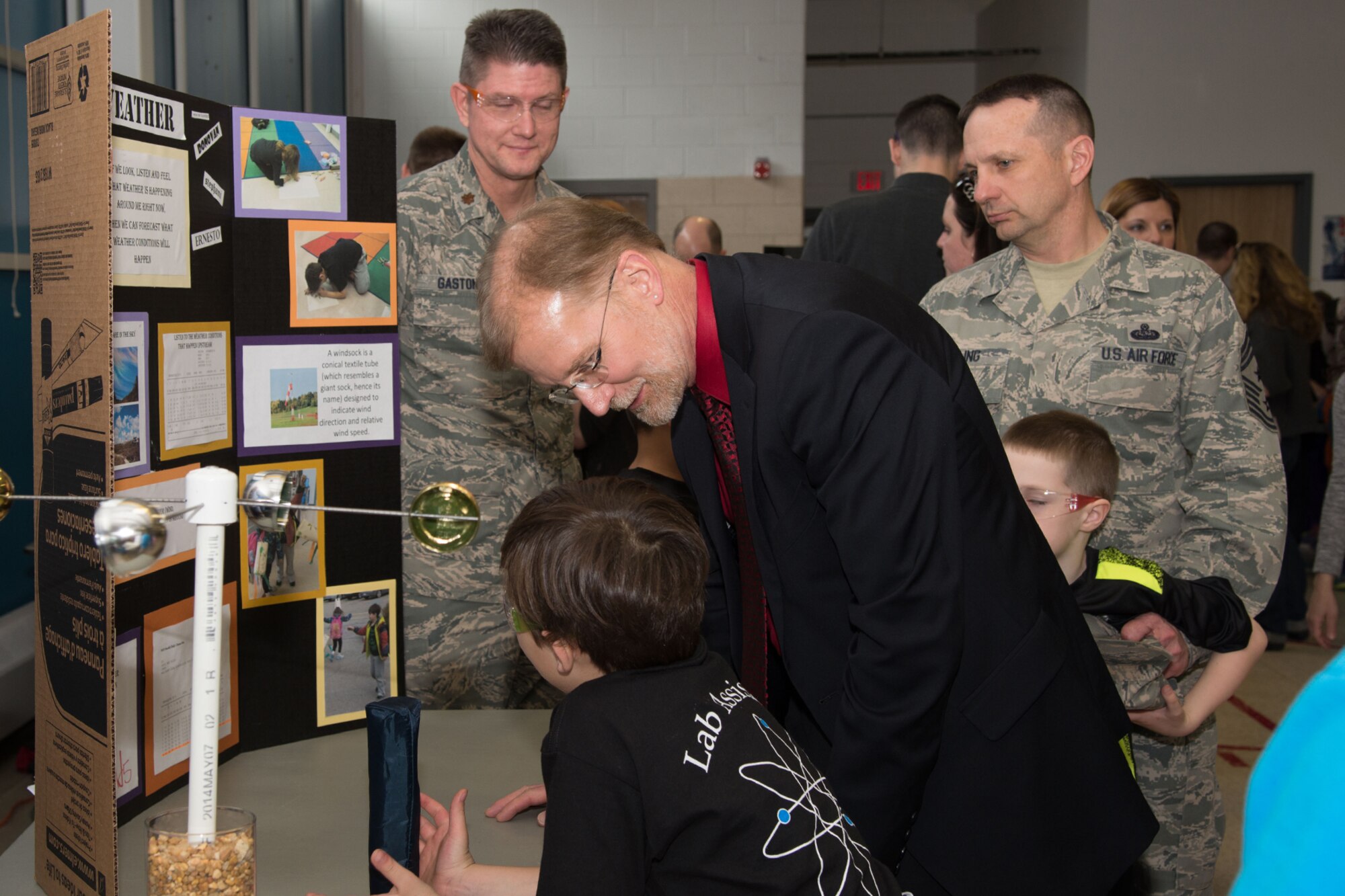 Steve Wert, Battle Management program executive officer, speaks with Donovan Hegner during a Hanscom Science Fair at the Primary School April 14, while the second grader's coach, Maj. Todd Gaston, and Command Chief Master Sgt. Craig A. Poling look on. Hegner’s team learned about climate and weather as part of their project. (U.S. Air Force photo by Mark Herlihy)