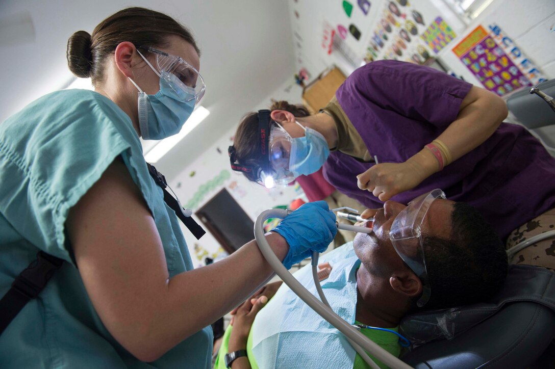 German army Lt. Col. Laura Dimovici and Petty Officer 3rd Class Gina Horsting perform a dental procedure at Hattieville Government School, one of two medical sites set up for Military Sealift Command hospital ship USNS Comfort to provide services during Continuing Promise 2015 in Hattieville, Belize, April 12, 2015. Both are assigned to the Naval Dental Clinic Camp Lejeune, Jacksonville, N.C.