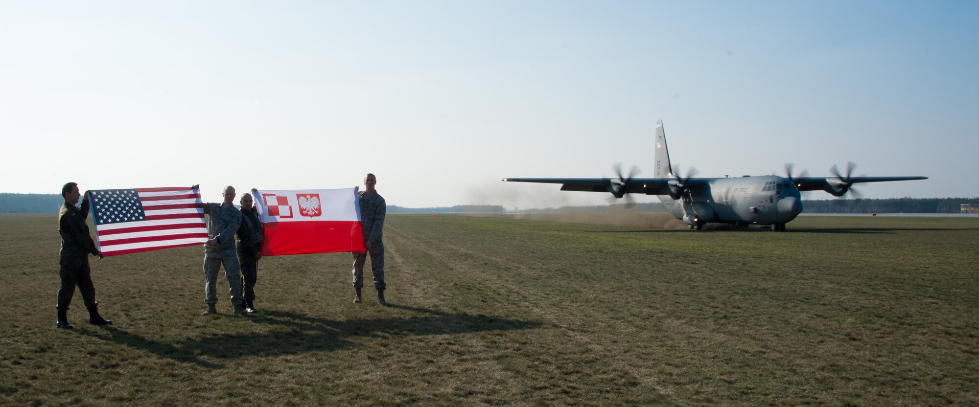 U.S. and Polish military members hold their country’s flag as a C-130J Super Hercules assigned to the 37th Airlift Squadron performs a grass-strip landing at Powidz Air Base, Poland, April 10, 2015. U.S. military members traveled to Powidz as part of a flying training deployment where they trained alongside their Polish counterparts. (U.S. Air Force photo/Senior Airman Jonathan Stefanko)