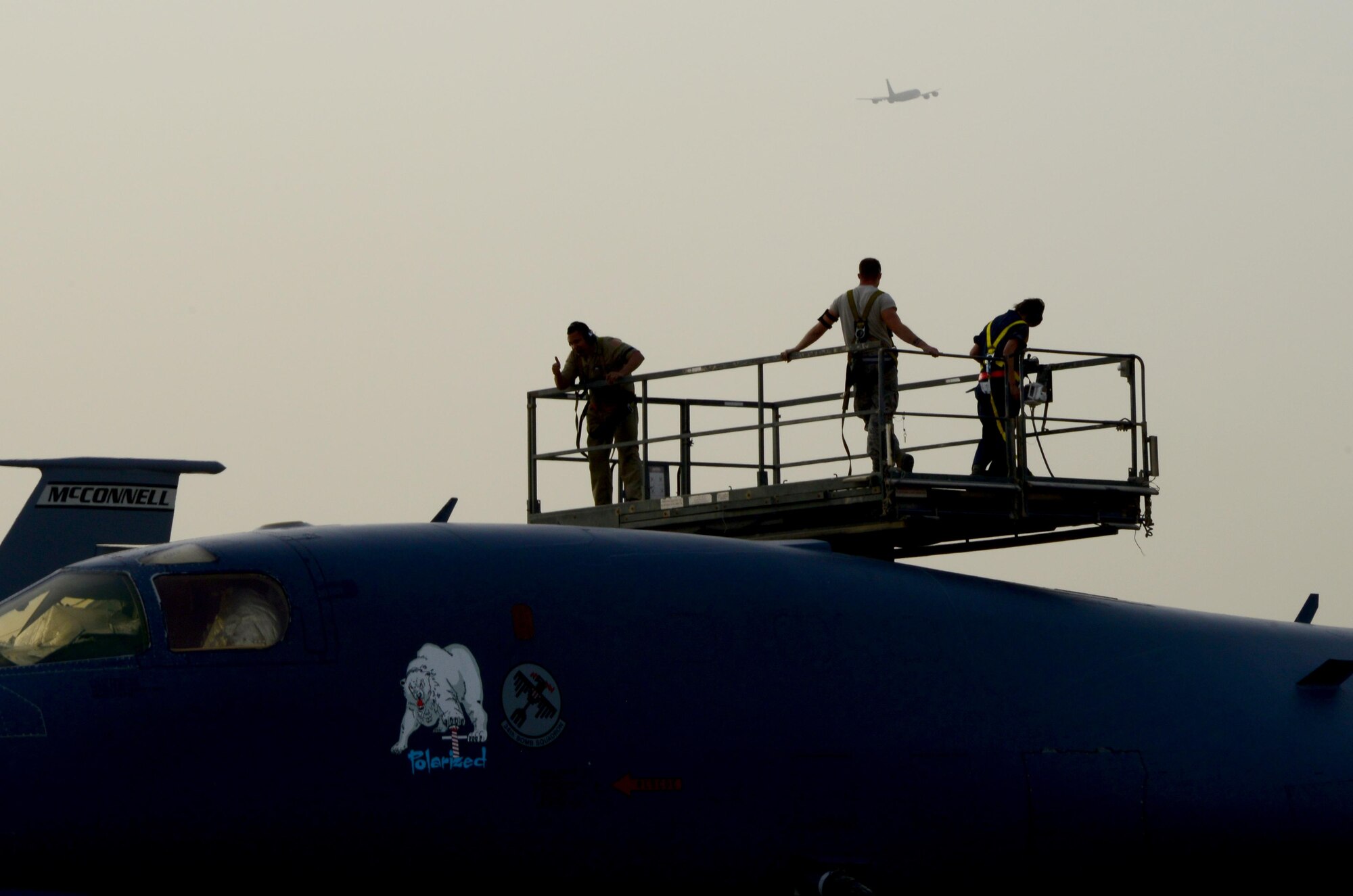 Airmen from the 379th Expeditionary Maintenance Group perform maintenance on a B-1B Lancer as a KC-135 Stratotanker takes off, April 8, 2015, at Al Udeid Air Base, Qatar. Airmen of the 379th Expeditionary Maintenance Group have worked around the clock to ensure aircraft and munitions are ready to go whenever and wherever they are needed. The continuous work of these maintenance Airmen ensured aircraft are constantly prepared for take-off, leading to over 1,600 sorties on average per month. (U.S. Air Force photo by Senior Airman Kia Atkins)