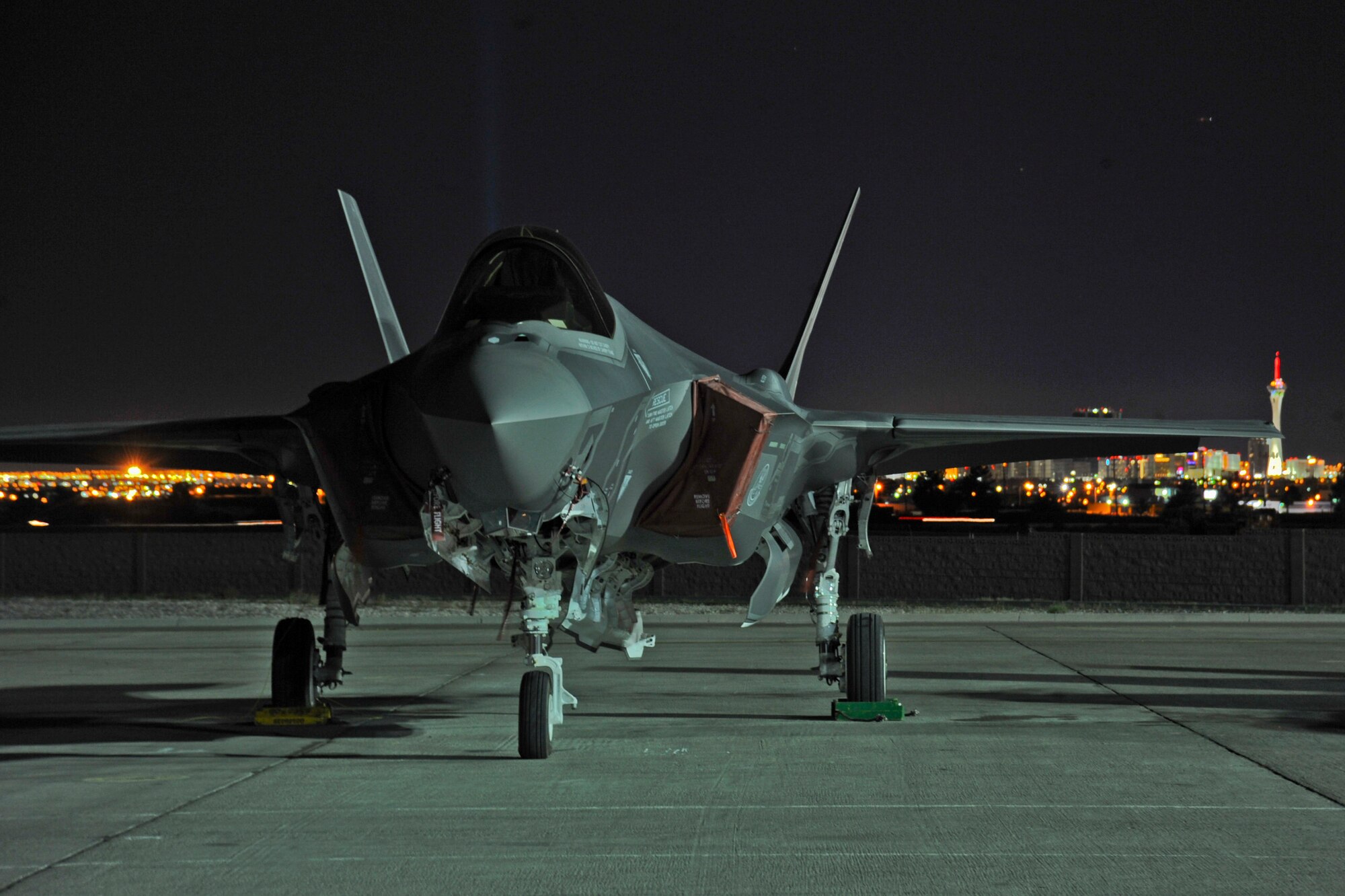 An F-35 from Luke Air Force Base rests on the Nellis AFB, Nevada, flightline April 8, 2015. The Las Vegas city lights are in the background. (U.S. Air Force photo by Staff Sgt. Darlene Seltmann)