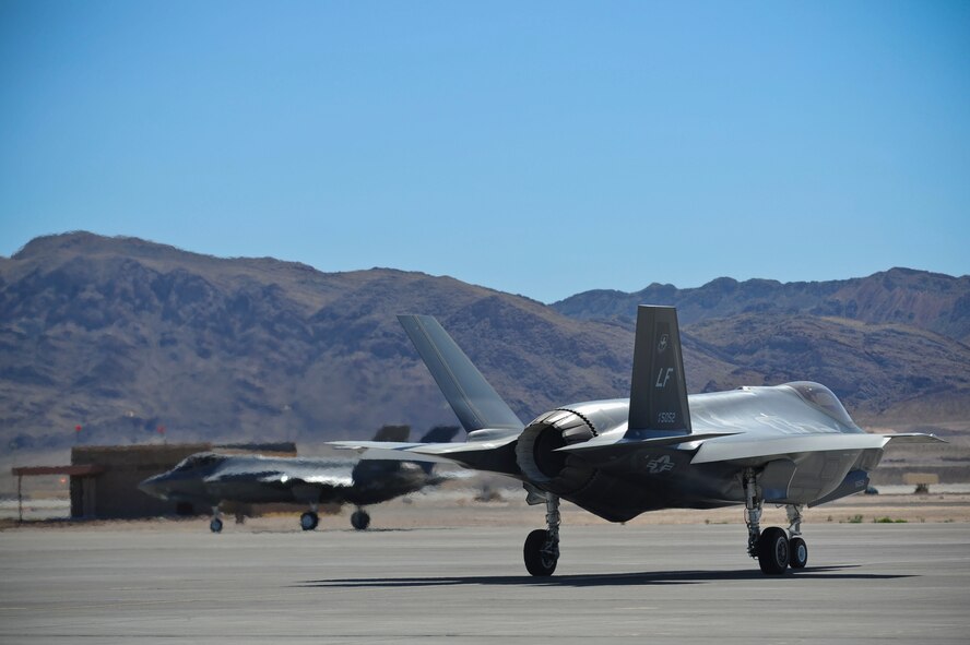 An F-35 from the Luke Air Force Base 61st Fighter Squadron’s “Top Dogs” speeds down the flightline as another of the unit’s Lightning IIs stands by for take off April 15, 2015 at Nellis AFB, Nevada. (U.S. Air Force photo by Staff Sgt. Darlene Seltmann)
