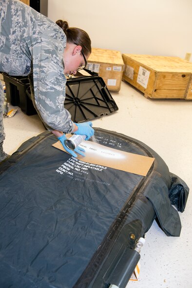 U.S. Air Force Senior Airman Jessica Burrell, 347th Operations Support Squadron aircrew flight equipment technician, labels an LRU-16/P one-man life raft with spray paint April 15, 2015, at Moody Air Force Base, Ga. Burrell documents the inspection date of the life raft prior to a six hour leakage test ensuring proper pounds per square inch standards for the flotation device. (U.S. Air Force photo by Airman Greg Nash/Released)  