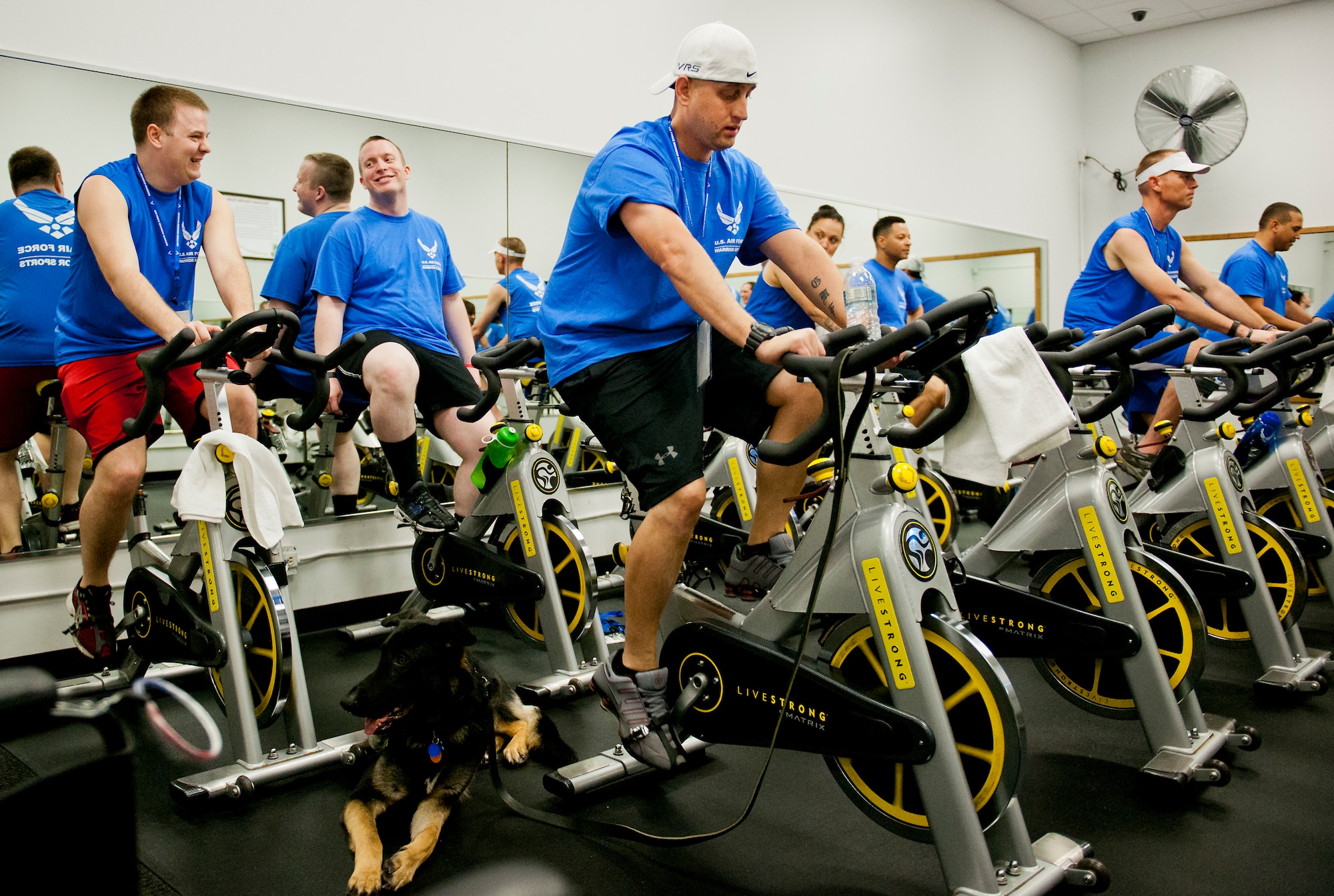 Senior Airman Chris Fugitt, a retired 96th Aircraft Maintenance Squadron Airman and an Air Force Wounded Warrior athlete, peddles through a spin class while his service dog, Rebel, takes a break during the first day of an introductory adaptive sports and rehabilitation camp at Eglin Air Force Base, Fla., April 13. Two years after complications from a massive stroke forced Chris to retire from the Air Force, his warrior spirit enabled him to power past a number of debilitating setbacks and attend his first camp.  (U.S. Air Force photo/Samuel King Jr.)