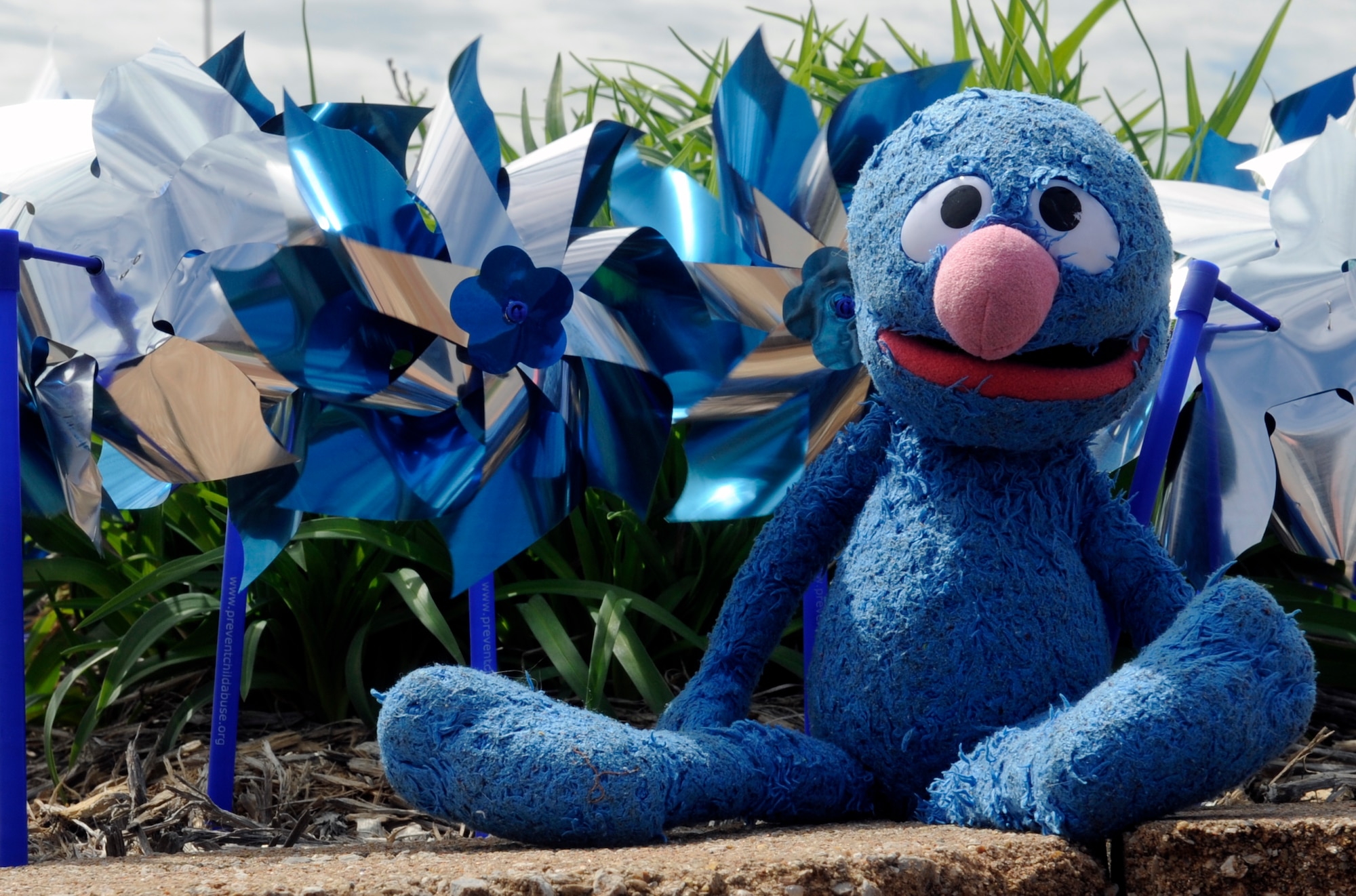 A stuffed animal of Grover from Sesame Street sits in front of blue and silver pinwheels at Whiteman air Force Base, Mo., April 14, 2015. Staff Sgt. Alexandra M. Longfellow, 509th Bomb Wing Public Affairs photojournalist, received Grover from a police officer on the night she was taken out of an abusive home.  April is Child Abuse Prevention Month and the pinwheel is a symbol for healthy starts for all children. (U.S. Air Force photo by Staff Sgt. Alexandra M. Longfellow/Released)