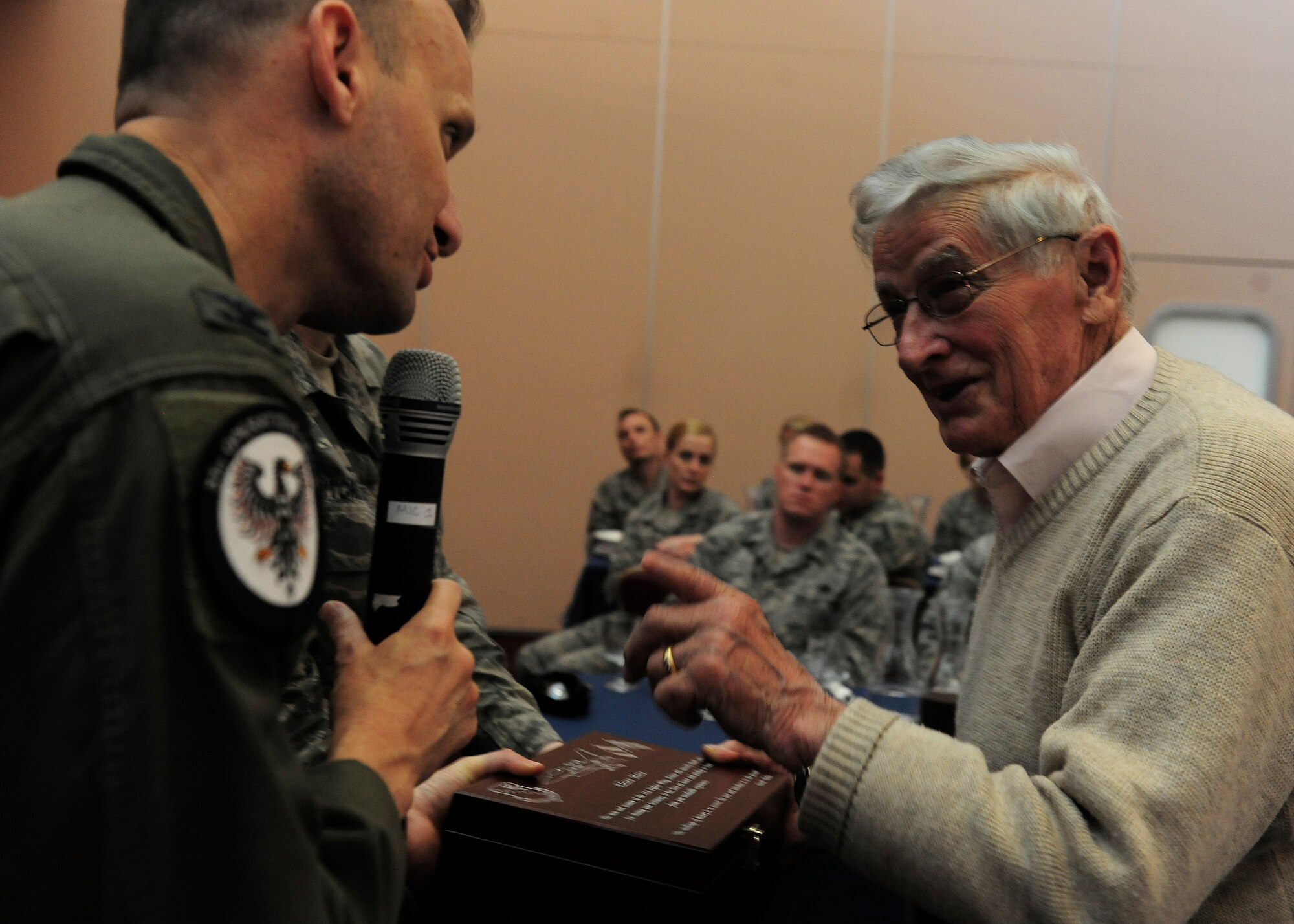 (From left) Col. Anthony Abernathy, 31st Operations Group commander hands  Eliseo Moro, a holocaust survivor, a plaque during a Holocaust Remembrance event April 13, 2015, at Aviano Air Base, Italy. Moro spoke with Airmen about his experience at Dachau concentration camp in Munich, Germany. (U.S. Air Force photo illustration by Staff Sgt. Evelyn Chavez/Released)