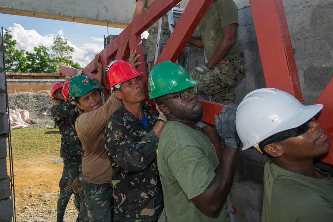 U.S. Marine engineers, assigned to the 9th Engineer Support Battalion, U.S. Navy Seabees, assigned to Naval Mobile Construction Battalion 5, and Armed Forces of the Philippines Army engineers from the 552nd Engineer Construction Battalion, lift a roof truss for placement at Don Joaquin Artuz Memorial Elementary School in Tapaz, Philippines, during Balikatan 2015, April 16. The engineers are part of the Joint Civil-Military Operations Task Force on the island of Panay constructing two
classrooms at the school. Balikatan, which means “shoulder to shoulder” in Filipino, is an annual bilateral training exercise aimed at improving the ability of Philippine and U.S. military forces to work together during planning, contingency, humanitarian assistance and disaster relief operations. (U.S. Navy photo by Chief Mass Communication Specialist Lowell Whitman/ Released)