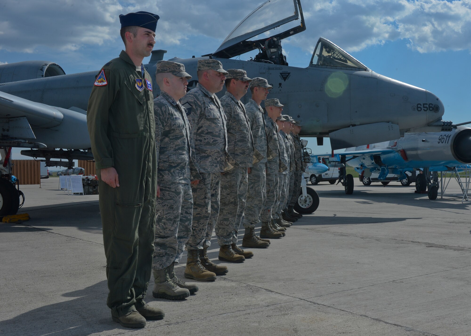 U.S. Air Force Airmen assigned to the 354th Expeditionary Fighter Squadron stand at attention next to static displays of a U.S. Air Force A-10 Thunderbolt II and a Romanian air force MiG-21 fighter jet before a media event on the flightline at Campia Turzii, Romania, April 16, 2015. About 200 Airmen and support equipment from the 355th Fighter Wing at Davis-Monthan Air Force Base, Arizona, and the 52nd Fighter Wing at Spangdahlem Air Base, Germany, will support the deployment in Campia Turzii. (U.S. Air Force photo by Staff Sgt. Joe W. McFadden/Released)