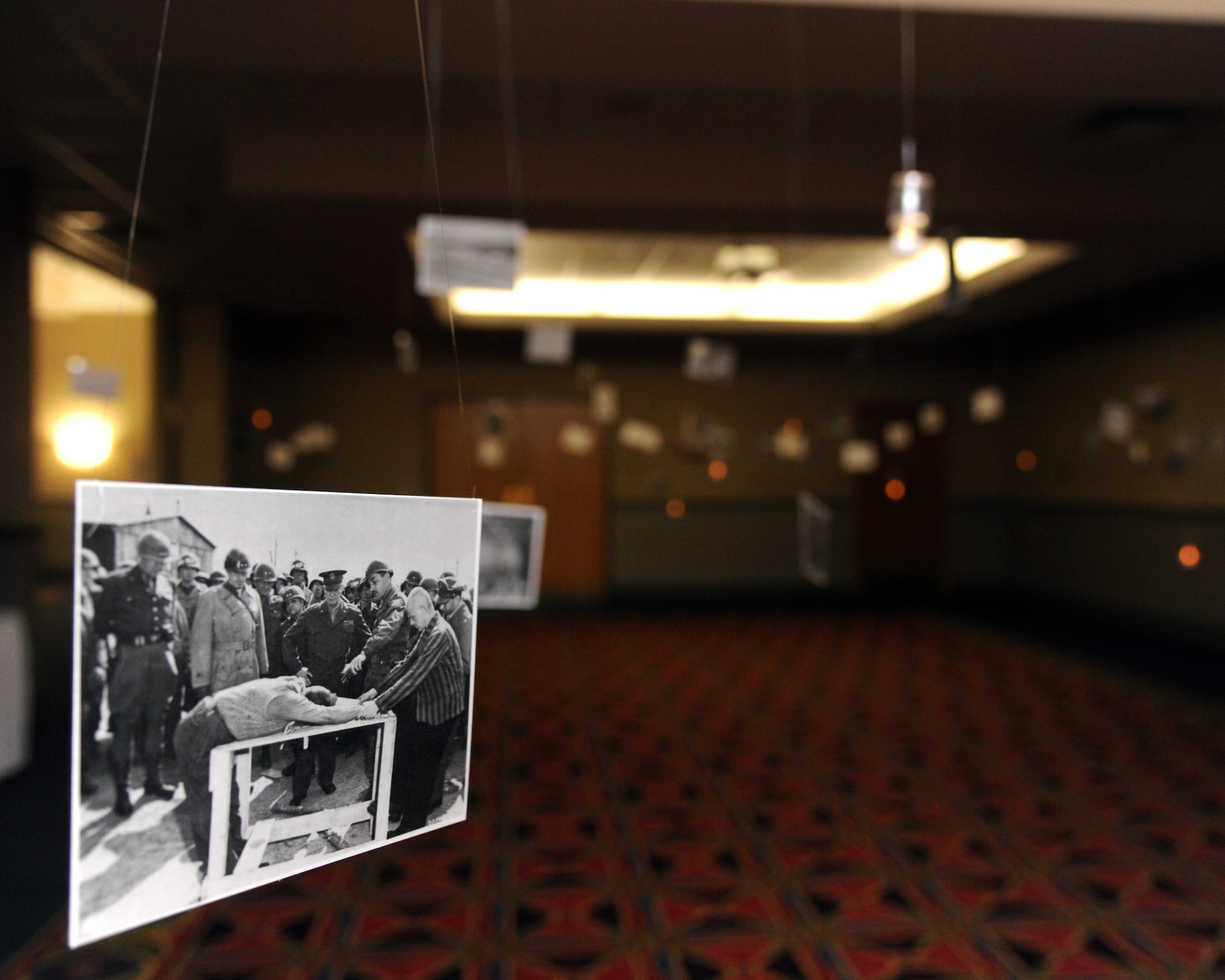 A display shows various images taken from numerous places in Germany during the Holocaust, depicting the horrific experiences that occurred during that time, Apr. 16, 2015 at the Northern Lights Club ballroom on Grand Forks Air Force Base, N.D. The pictures hung from the ceiling, surrounded by hanging electronic candles giving off an unsettling vibe as patrons walked through to witness past atrocities. (U.S. Air Force photo by Senior Airman Zachiah Roberson/released)