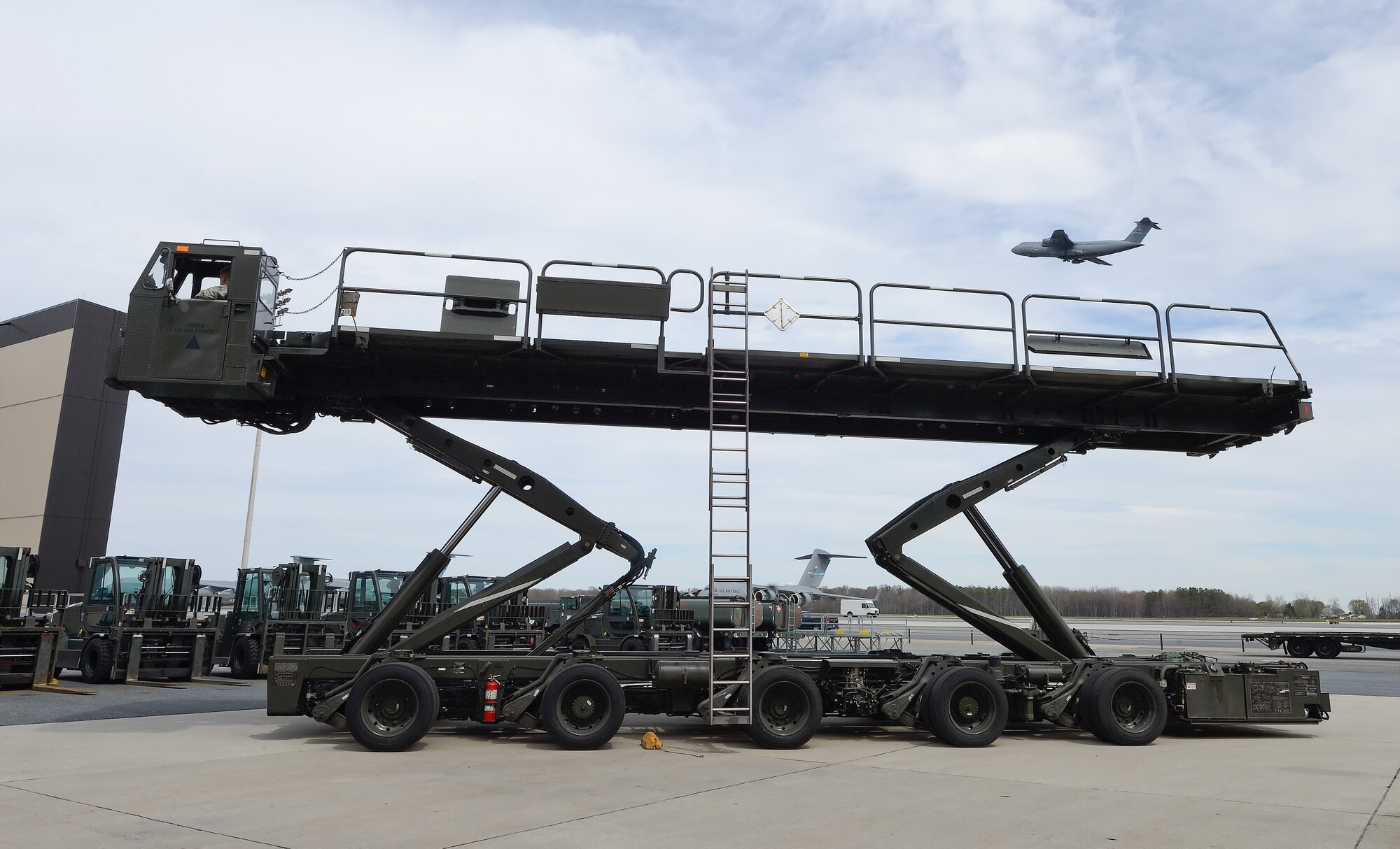 A 60K 'Tunner' cargo transport and loading vehicle elevates itself during a capabilities demonstration for the 2015 Dover Air Force Base Honorary Commanders tour of the 436th Maintenance Group April 15, 2015, on Dover AFB, Del., while a C-5M Super Galaxy passes by in the background. The cargo loader is commonly known as a 'Tunner' in honor of Lt. Gen. William H. Tunner, an enterprising advocate and pioneer of early Air Force air cargo movement and operations. (U.S. Air Force photo/Greg L. Davis)