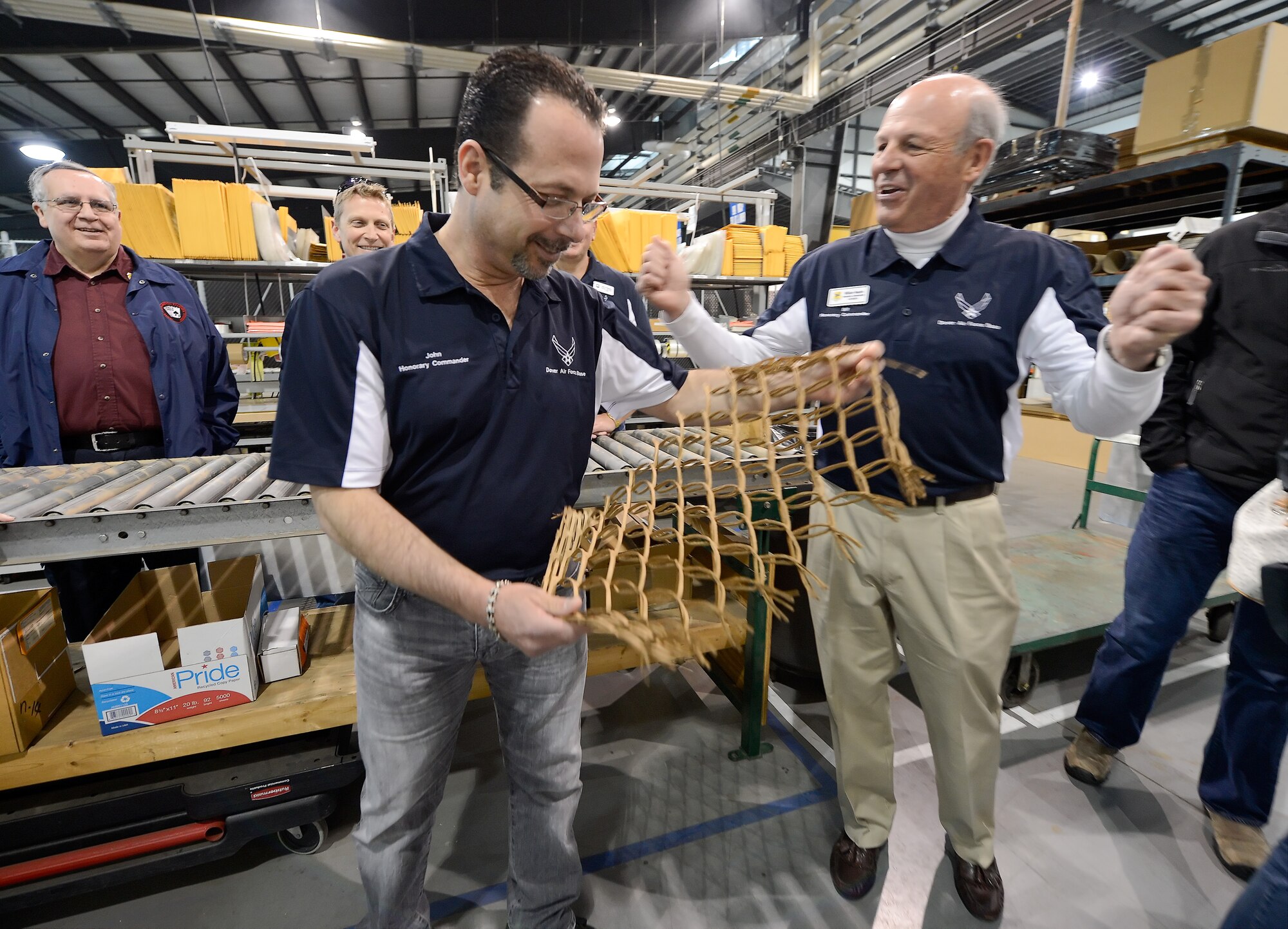 John Yoho, 436th Aerial Port Squadron honorary commander, stretches a piece of cardboard that has been shredded and turned in to packing material inside of Dover's Super-Port facility while Bill Neaton, 436th Medical Operations Squadron honorary commander, encourages him to stretch it further April 15, 2015, on Dover Air Force Base, Del. The 2015 Dover AFB Honorary Commanders toured the 436th Maintenance Group to better understand the units??? mission and capabilities. (U.S. Air Force photo/Greg L. Davis)
