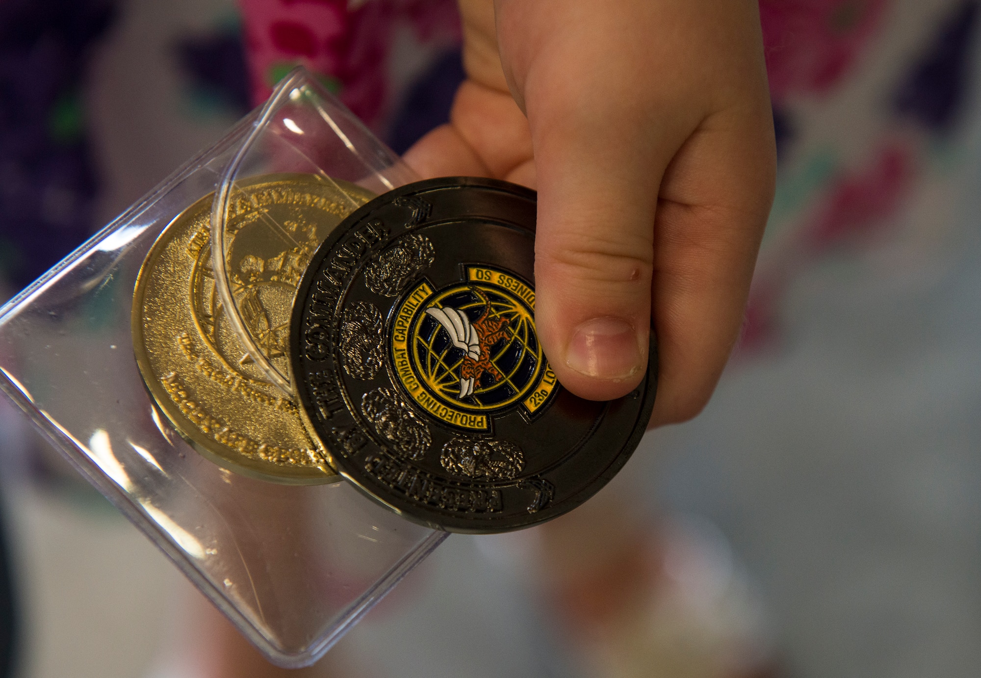 Madison, daughter of U.S. Air Force Staff Sgt. Jonathan Rhodes, 23d Logistics Readiness Squadron, grips two coins during a surprise redeployment April 14, 2015, at Moody Air Force Base, Ga. The 23d LRS presented Madison with a certificate and two coins for displaying courage and continued resilience during her father’s deployment. (U.S. Air Force photo by Airman 1st Class Ceaira Tinsley/Released)
