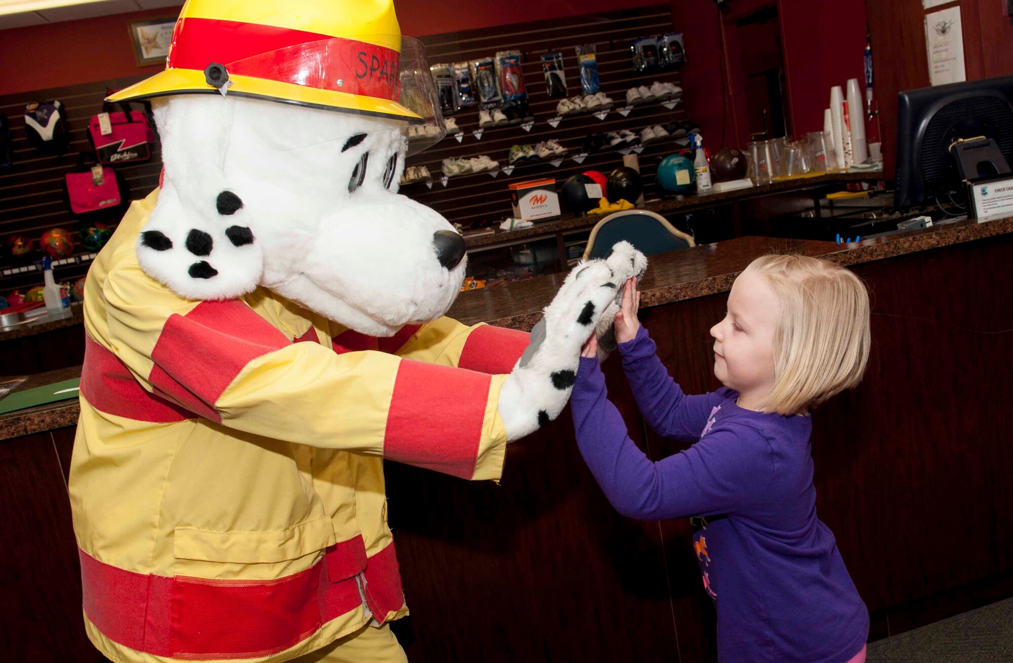 Blakeley Shepherd, age 4, high-fives Sparky the fire dog on Minot Air Force Base, N.D., April 15, 2015. A celebration was hosted at Rough Rider Lanes to show appreciation toward military children. (U.S. Air Force photo/Airman 1st Class Sahara L. Fales)
