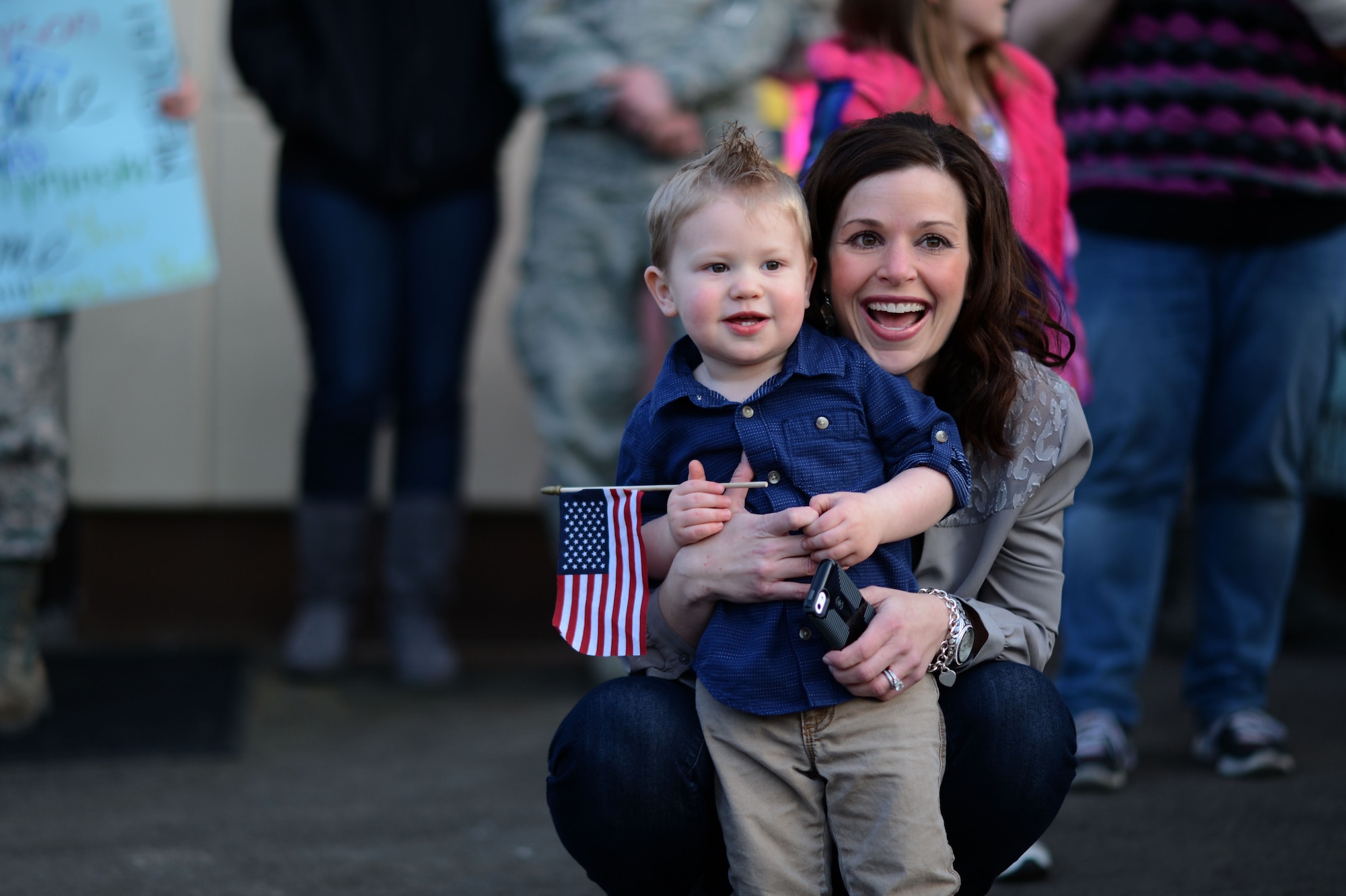 A 606th Air Control Squadron family smile as a bus approaches during a deployment homecoming on Spangdahlem Air Base, Germany, April 17, 2015. The deployed members supported Operations Enduring Freedom, Inherent Resolve, Resolute Support, Freedom’s Sentinel, and the combined defense of the Arabian Gulf. (U.S. Air Force photo by Senior Airman Gustavo Castillo/Released) 