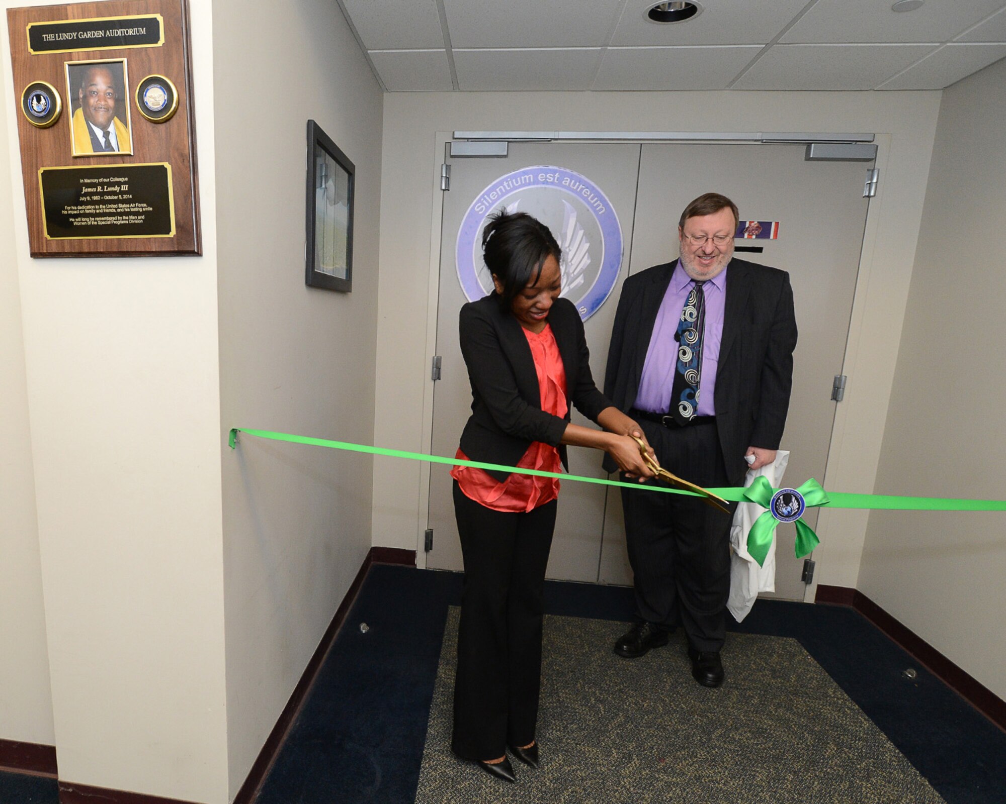 Emerald Lundy cuts the ribbon rededicating the Garden Auditorium as the Lundy-Garden Auditorium as Steven Cote, Special Programs Division deputy director, looks on during a ceremony in Building 1614, April 16. Emerald’s father, James R. Lundy III, passed away suddenly late last year and had been a long time employee at Hanscom. (U.S. Air Force photo by Jerry Saslav)