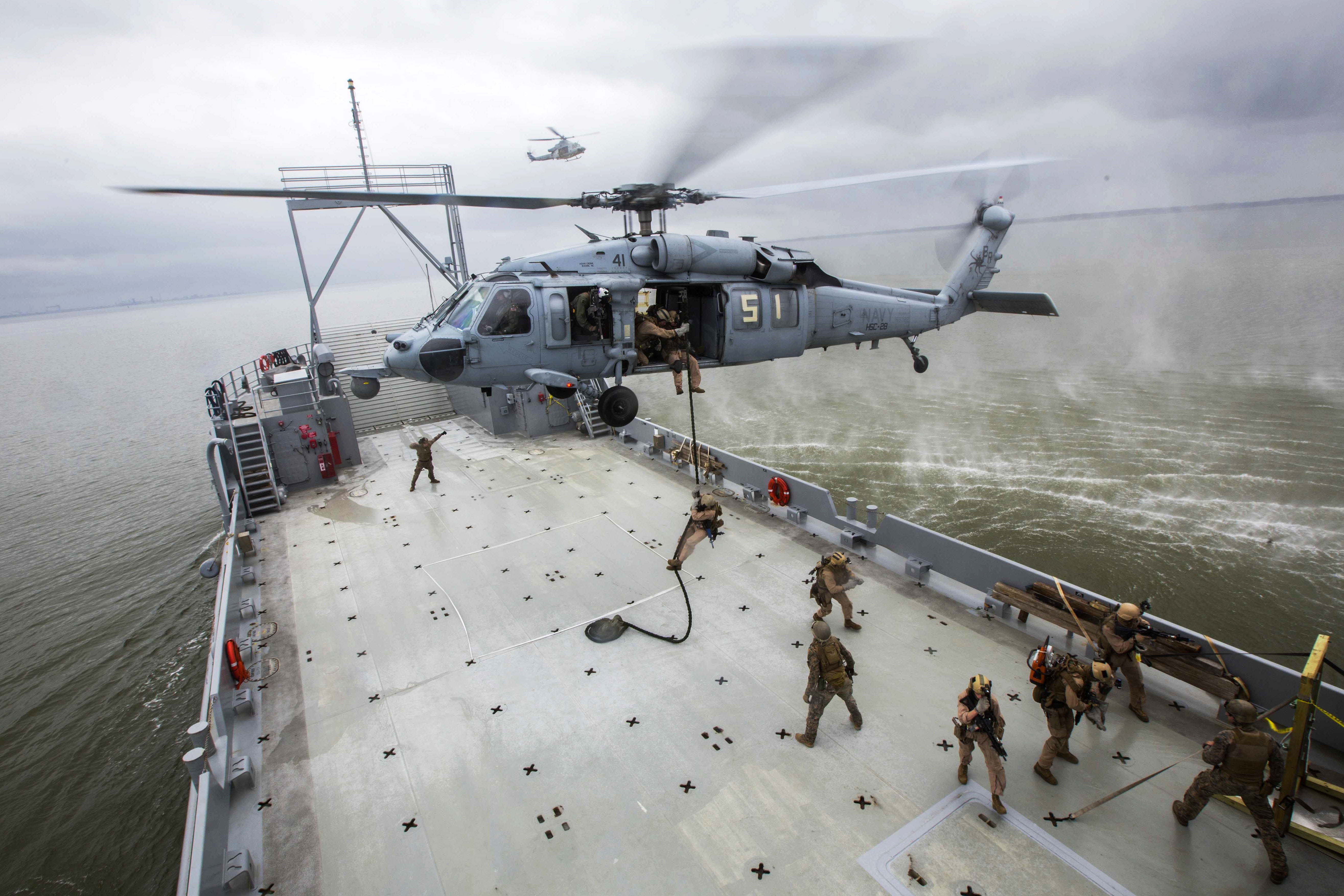 Marines fast rope from an SH 60 Seahawk helicopter onto a ship during