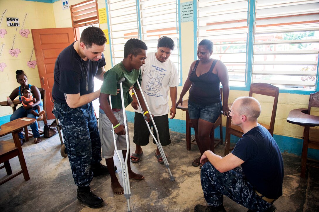 U.S. Navy Petty Officer 3rd Class Kevin Banta, left, a physical therapy technician assigned to the Naval Medical Center in Portsmouth, Va., and Lt. Philip Burgees, a  physical therapist at the same center, teach a Belizean child how to use crutches at the Independence Polyclinic during Continuing Promise 2015 in Independence, Belize, April 13, 2015.