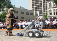 Senior Airman Corey Mcenery, 502nd Civil Engineer Squadron Explosive Ordnance Disposal technician at Joint Base San Antonio-Lackland, demonstrates the uses of a bomb suit and robot as part of bomb disposal procedures during Air Force at the Alamo events in conjunction with Fiesta San Antonio April 20.  The suit weighs about 80 pounds and protects Airmen from explosives at an arm’s length, or roughly three feet.  The robot is used to keep Airmen safe at a greater distance and can be used to inspect and remove a suspicious package.  (U.S. Air Force photo by Melissa Peterson/released)