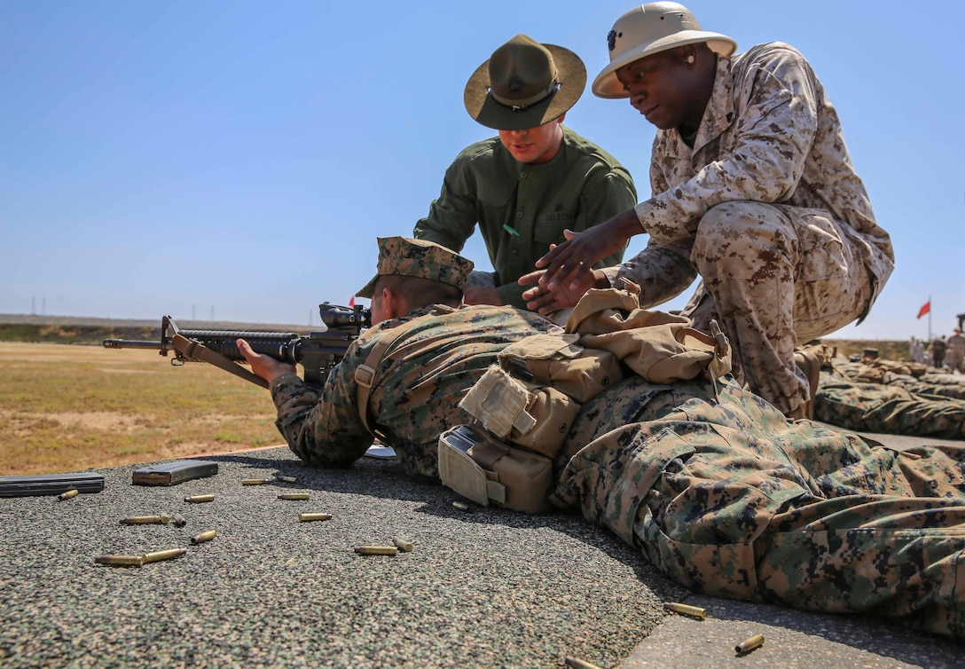 Corporal Hector F. Deleon (left), primary marksmanship instructor, and Cpl. Tony Williams, range coach, Range Company, Weapons and Field Training Battalion, assist a recruit of Kilo Company, 3rd Recruit Training Battalion, in improving his next shot during rifle week at Edson Range, Marine Corps Base Calif., April 14. The PMIs spend every day for two weeks with the recruits making sure they are comfortable with their weapons and understand the fundamentals of marksmanship. Today, all male recruits recruited from recruiting stations west of the Mississippi are trained at MCRD San Diego. The depot is responsible for training more than 16,000 recruits annually. Company K is scheduled to graduate from recruit training on May 29.