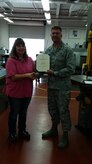 Major Brian Clark, 437th Maintenance Squadron commander presents Anna Hill, 437th MXS Metals Technology supervisor with her 2015 Volunteer Excellence Award for Joint Base Charleston in the Metals Technology shop, April 17, 2015 at JB Charleston. Hill  was recognized for her leadership and volunteerism with the Boy Scouts of America.This award is authorized by the U.S. Air Force Chief of Staff, for federal civilians, family members, military retirees, and federal retirees who perform outstanding volunteer community service.  It is designed to recognize exceptional long term community support and not a single act or achievement. (Courtesy photo)