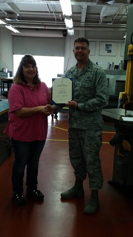 Major Brian Clark, 437th Maintenance Squadron commander presents Anna Hill, 437th MXS Metals Technology supervisor with her 2015 Volunteer Excellence Award for Joint Base Charleston in the Metals Technology shop, April 17, 2015 at JB Charleston. Hill  was recognized for her leadership and volunteerism with the Boy Scouts of America.This award is authorized by the U.S. Air Force Chief of Staff, for federal civilians, family members, military retirees, and federal retirees who perform outstanding volunteer community service.  It is designed to recognize exceptional long term community support and not a single act or achievement. (Courtesy photo)