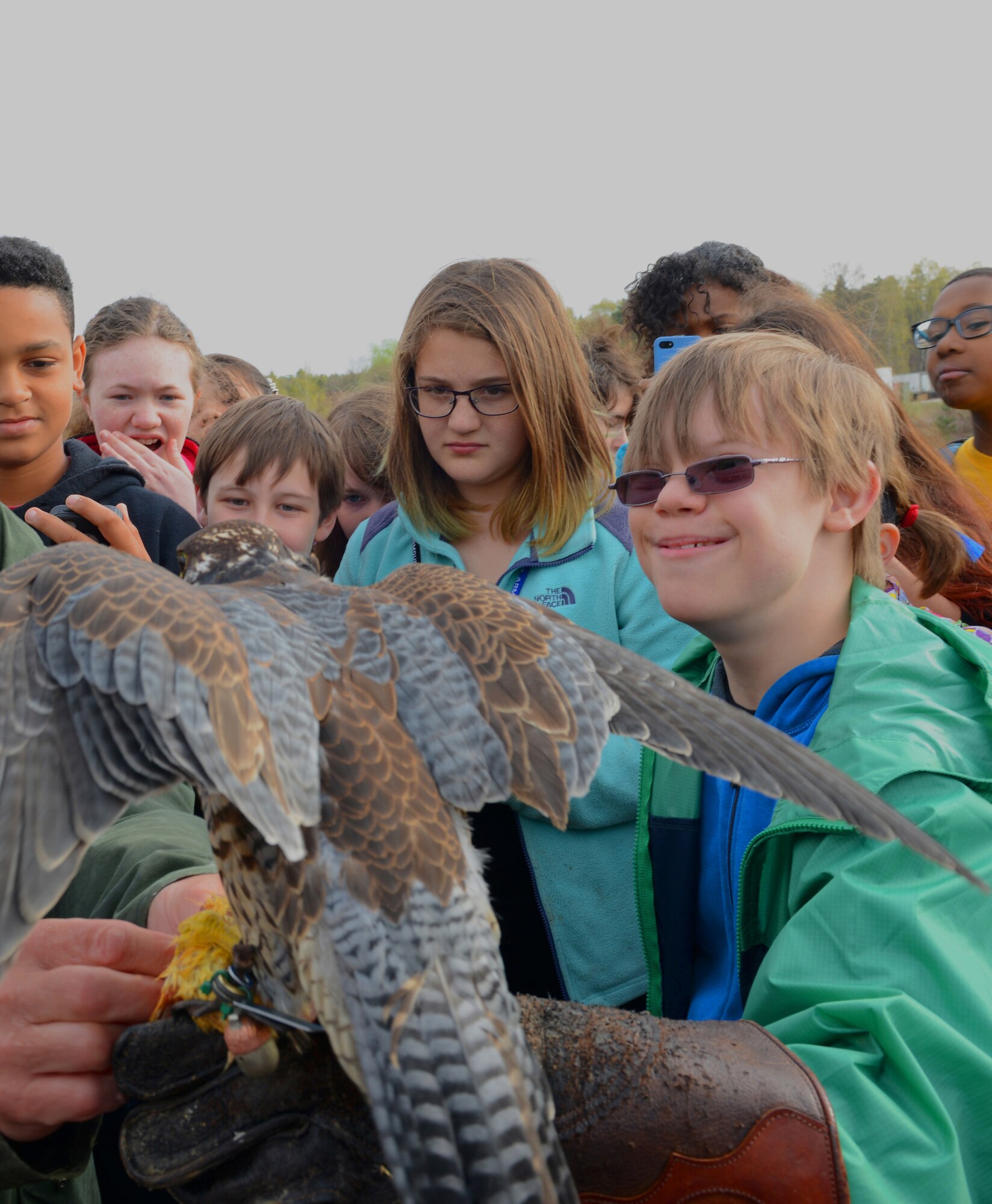 A falconer with the 86th Airlift Wing Flight Safety Office assists a sixth-grade student from Ramstein Middle School with putting on a leather glove to hold and feed a peregrine falcon as a part of the Bird Aircraft Strike Hazard demonstration presented for Earth Day April 16, 2015, at Ramstein Air Base, Germany. The show demonstrated to the students how the falcons dive to catch their prey and explained how they are used to prevent other birds from interfering with planes that are taking off or landing on the flightline.  (U.S. Air Force photo/Airman 1st Class Tryphena Mayhugh)
