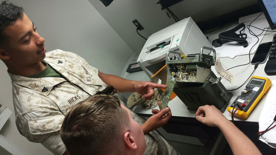 Cpl Carl J. Hicks, a personal computer technician, helps LCpl Dylan T. Hunt troubleshoot an AN/GRA93B for Ground Communications Maintenance Section.