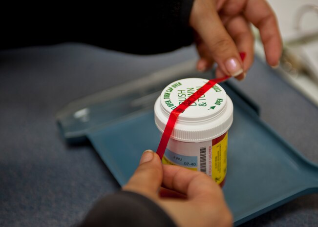 A volunteer at the satellite pharmacy places a red label on a prescription bottle at Nellis Air Force Base, Nev., April 17, 2015. At the satellite pharmacy, civilians volunteer over 240 hours a week to help support operations and the overall health of patients. (U.S. Air Force photo by Airman 1st Class Jake Carter)