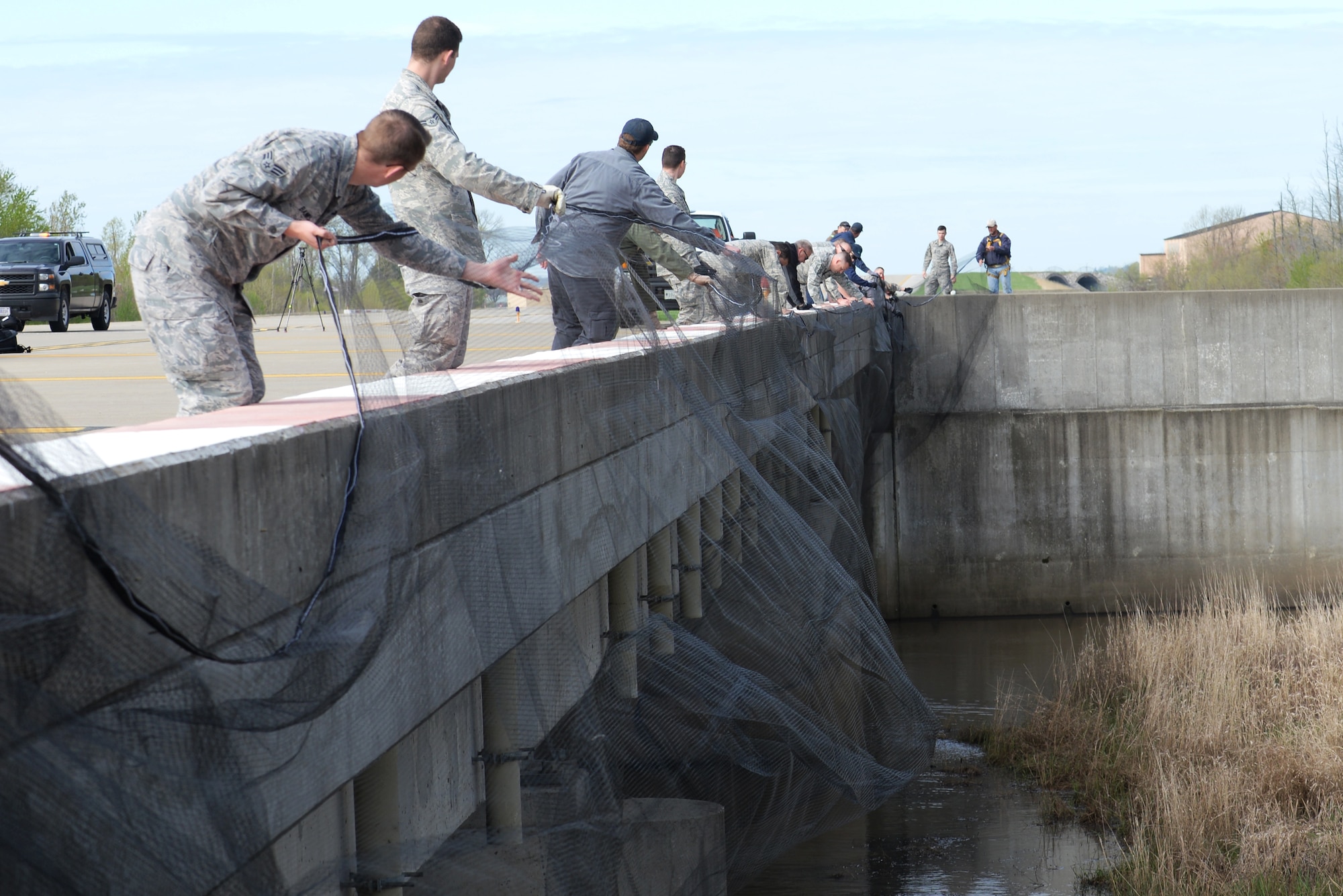 Members from the 375th Safety Office, the 375th Operations Squadron, Mid-America Airport and the United States Department of Agriculture throw netting over a bridge on the flight line at Scott Air Force Base, Illinois April 15. The bird netting is being used to prevent cliff swallows from nesting there and ultimately reduce bird strikes. (U.S. Air Force Photo by Airman 1st Class Megan Friedl)