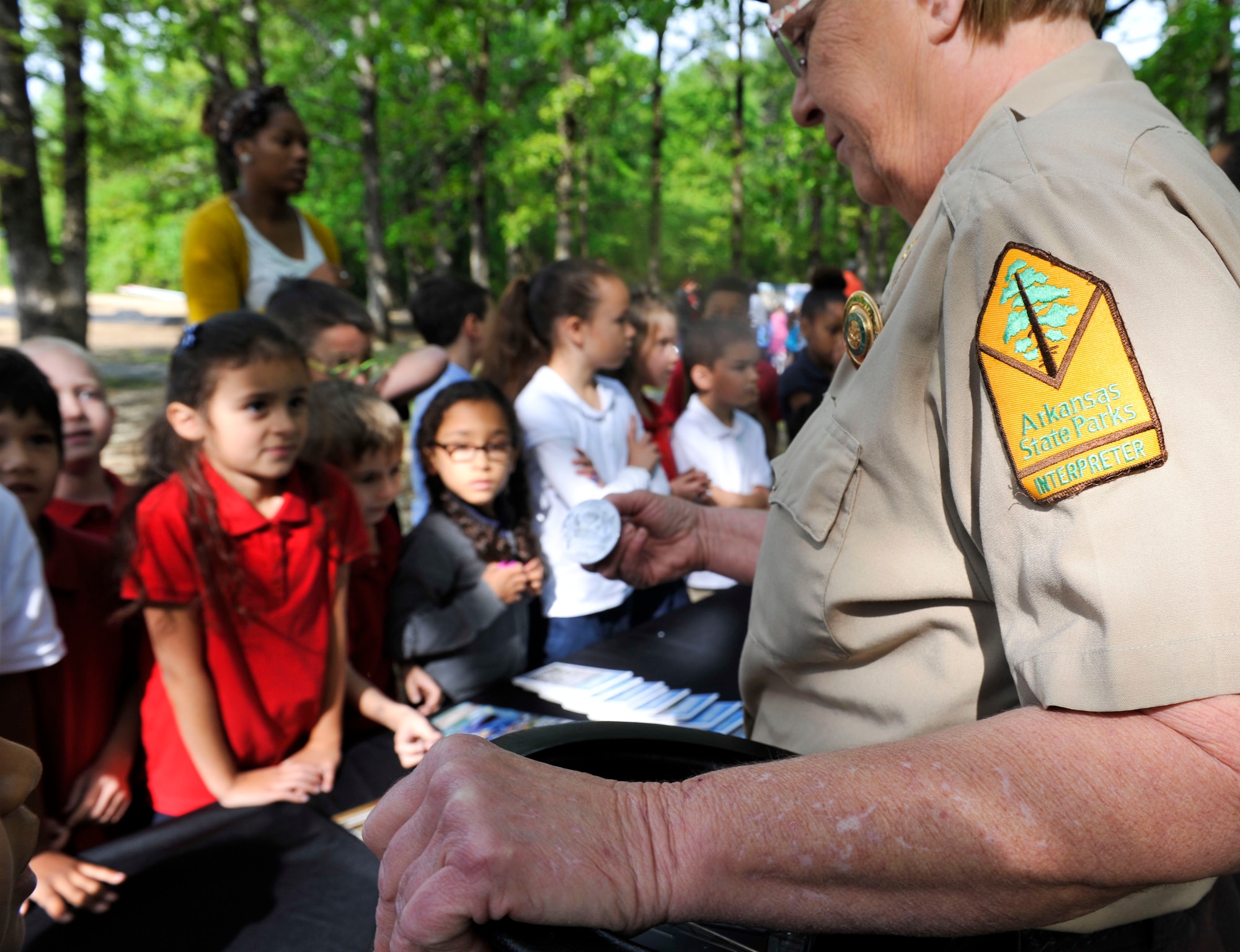 Betty Coors, an Arkansas State Parks representative, shows Arnold Drive Elementary School students  a state park pin April 22, 2015. The school celebrated Earth Day’s 45 th anniversary by having the students walk through a nature trail with several learning exhibits around. (U.S. Air Force photo by Senior Airman Regina Edwards)