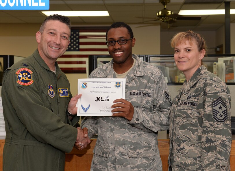 Staff Sgt. Malcolm Williams, center, 47th Force Support Squadron NCO in charge of Assignments and Formal Training, poses with Col. Brian Hastings, 47th Flying Training Wing commander, and Chief Master Sgt. Teresa Clapper, 47th FTW command chief, after accepting the XLer of the Week award here April 15, 2015. The XLer is a weekly award chosen by wing leadership and is presented to those who consistently make outstanding contributions to their unit and Laughlin. (U.S. Air Force photo by Airman 1st Class Ariel D. Delgado)(Released)